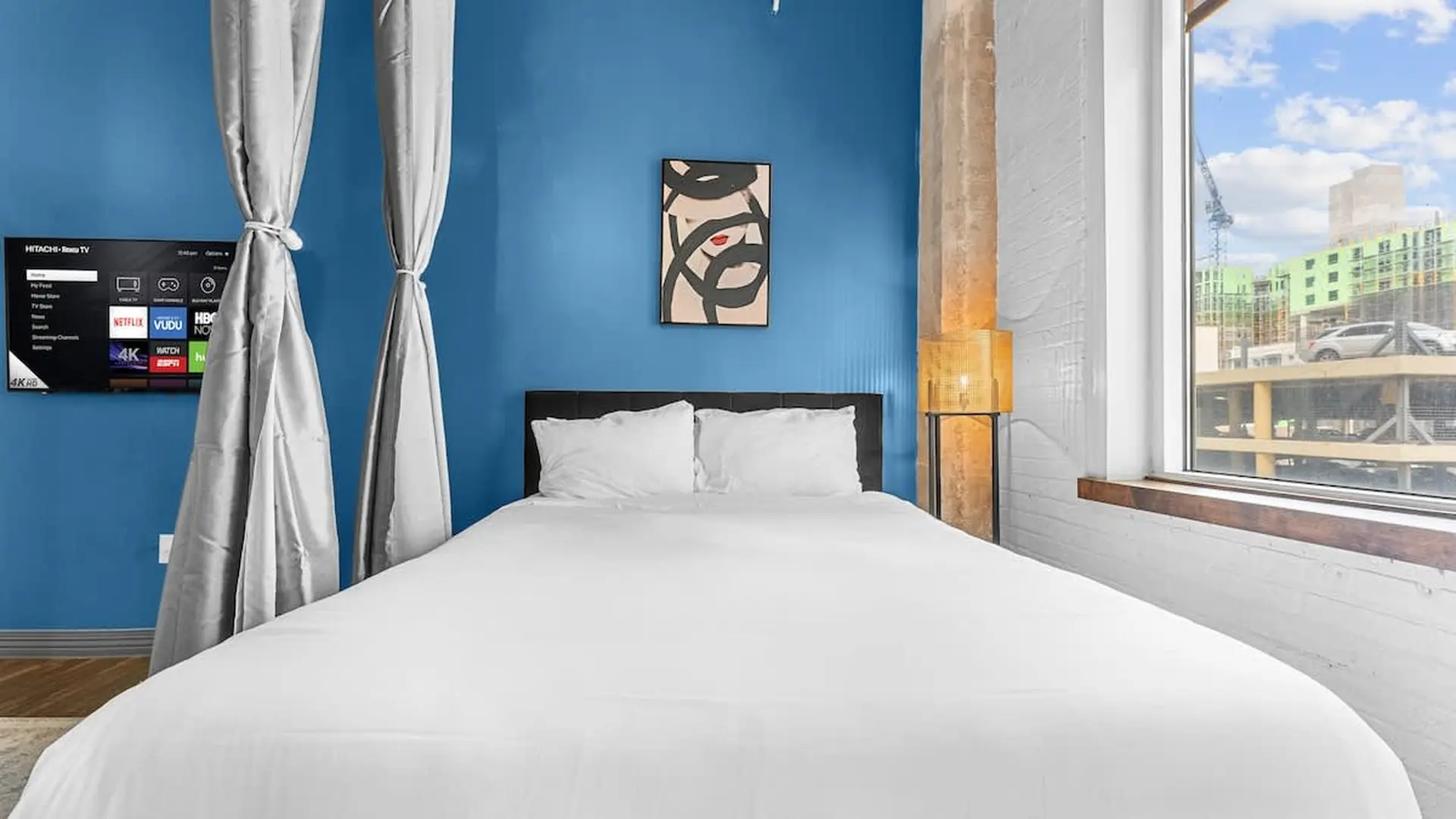 A bed with white linens is in front of a blue wall and a window.