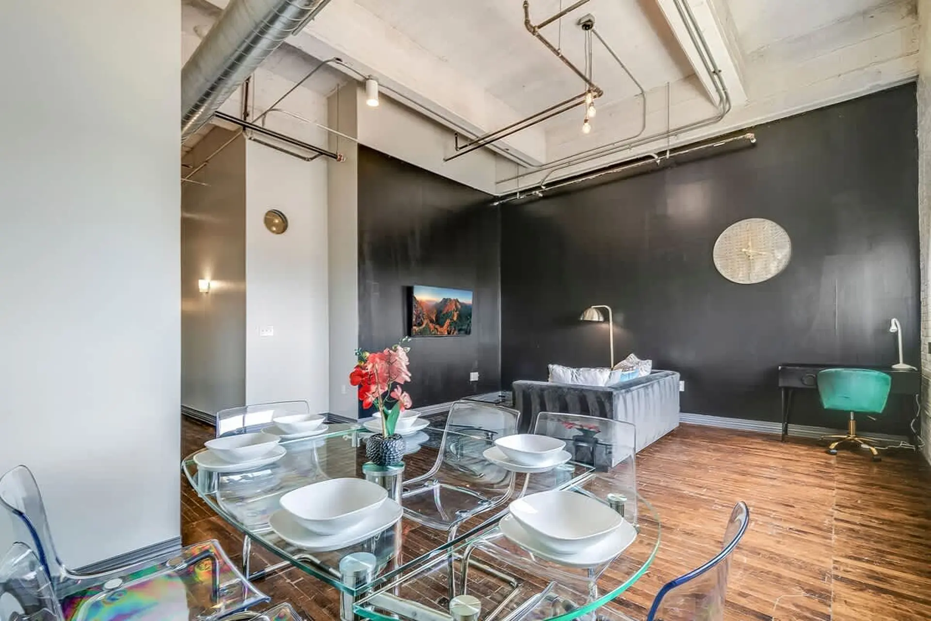 An industrial-style dining and living area with a glass table and chairs.
