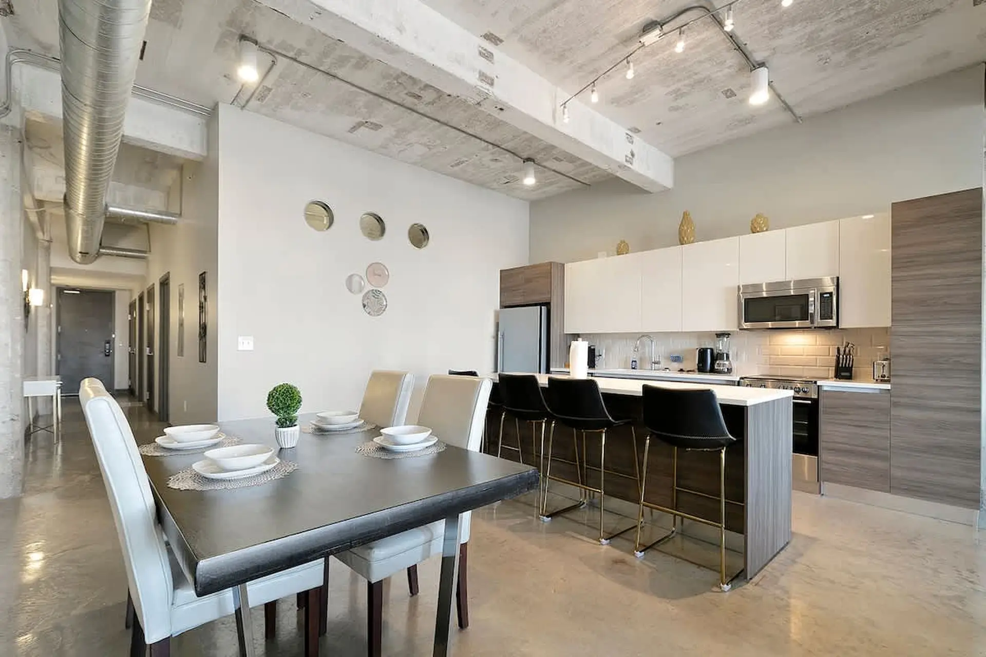 Modern dining and kitchen area with sleek furniture and industrial-style ceiling.