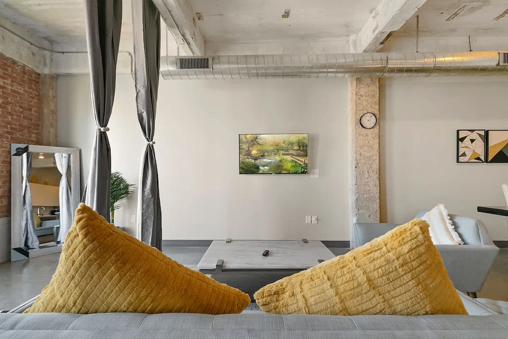 Two yellow pillows rest on a gray couch, in front of a TV and artwork.
