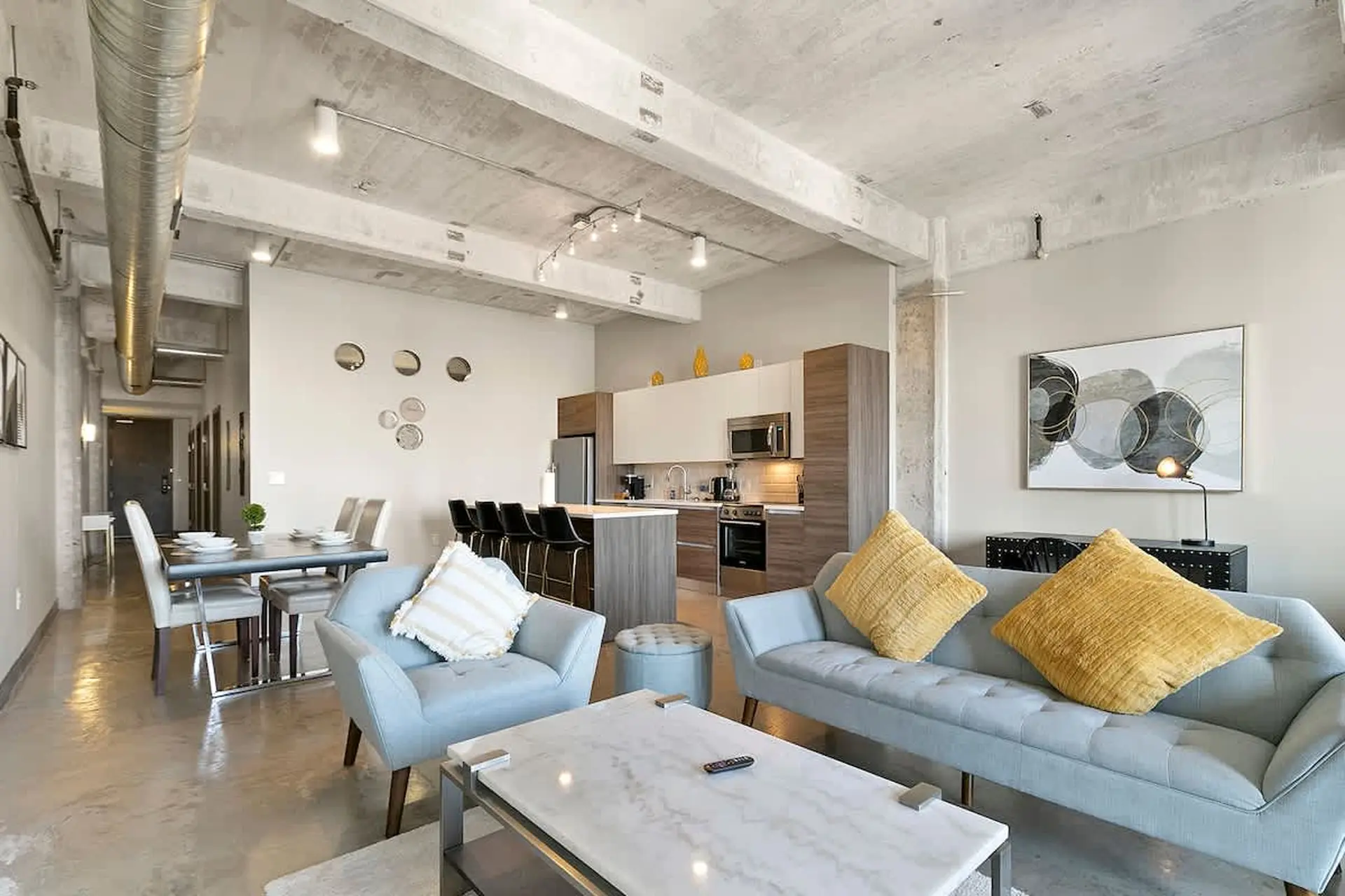 A modern living room and kitchen with concrete ceilings, a blue couch, and a marble coffee table.