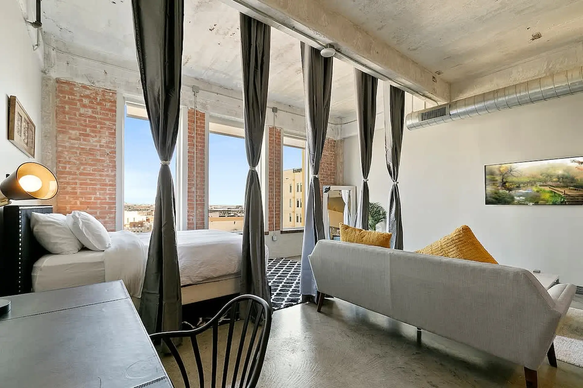 Loft bedroom with bed, desk, couch, and artwork on the wall.