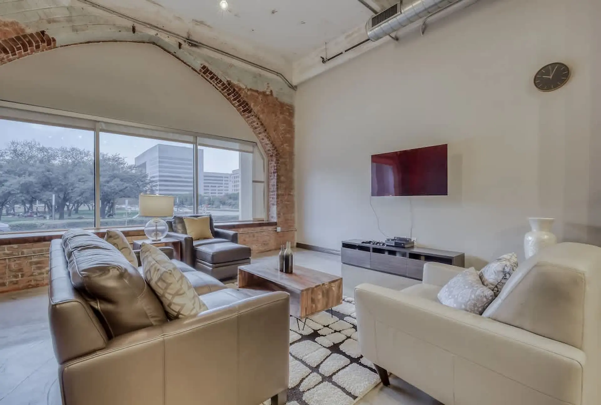 A living room with exposed brick, modern furniture, and a large window overlooking buildings.