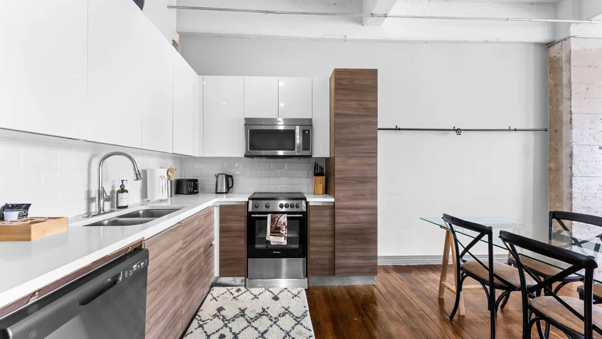 A modern kitchen with white cabinets, a stainless steel microwave and oven, and a small dining table