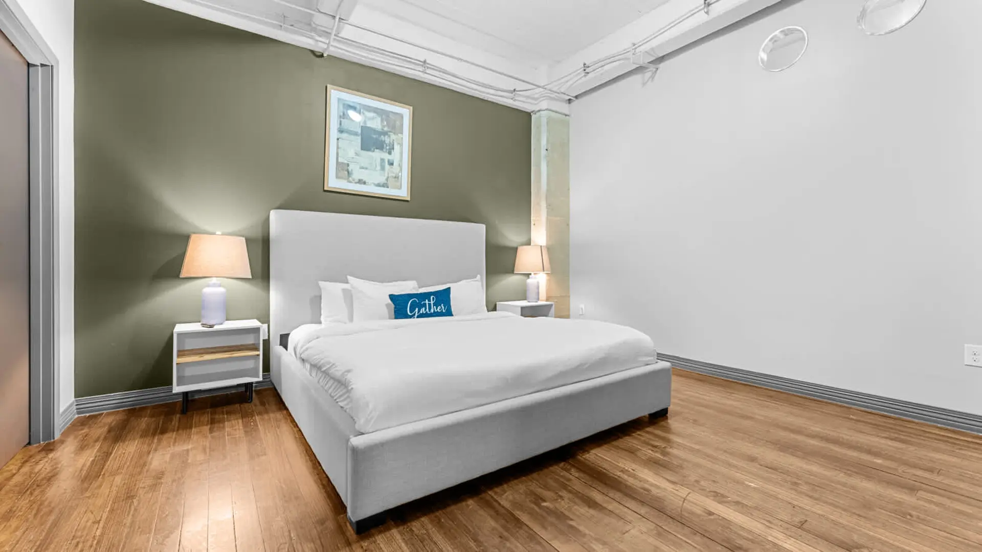 Bedroom with a king-size bed, bedside tables, lamps, and artwork on a green accent wall.