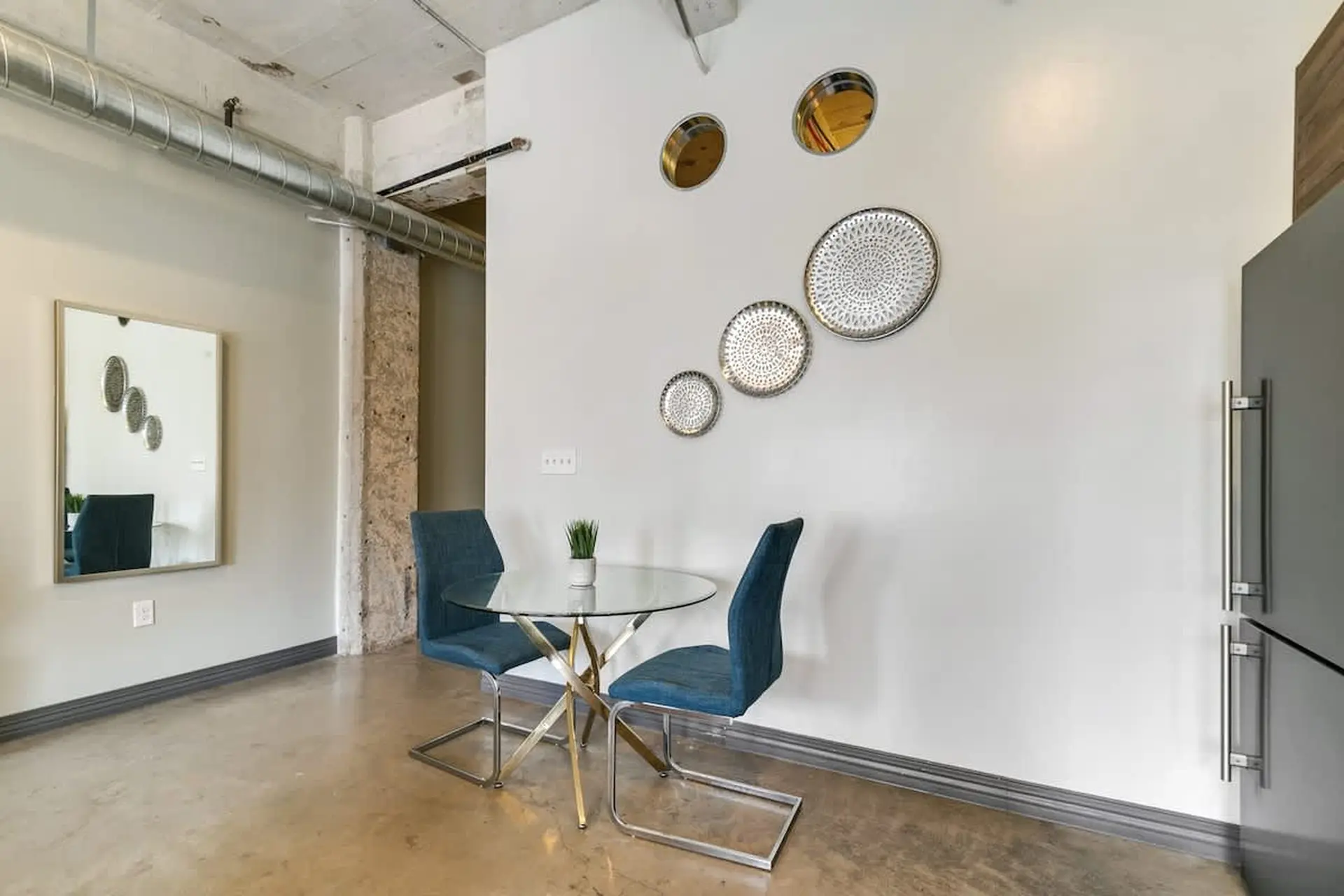 A modern dining set with a glass table, two blue chairs, and wall decor.