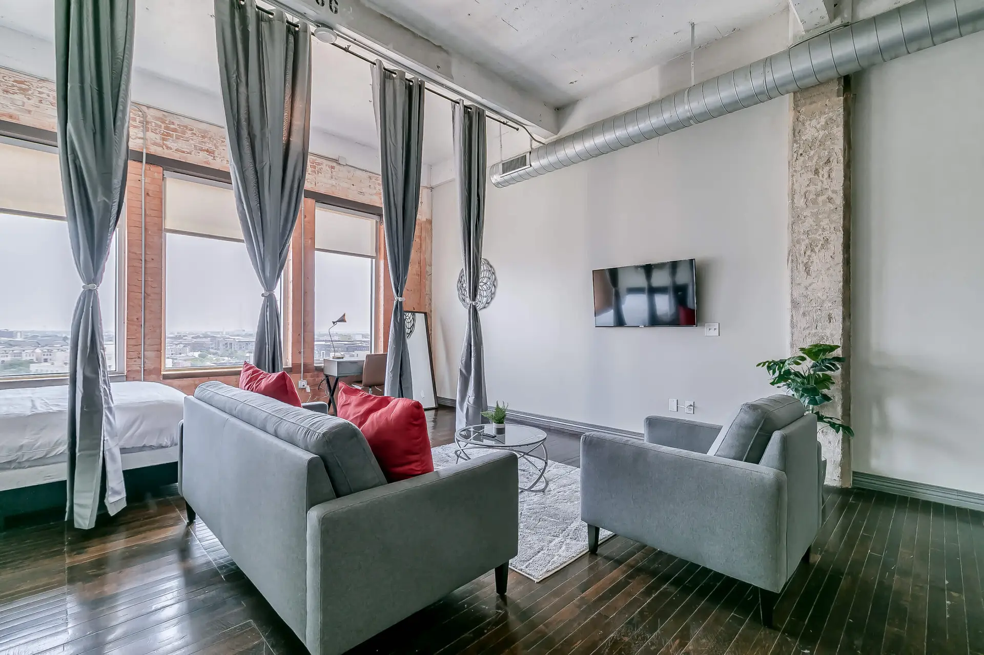 A loft living room with two gray sofas, red pillows, a coffee table, and a TV.