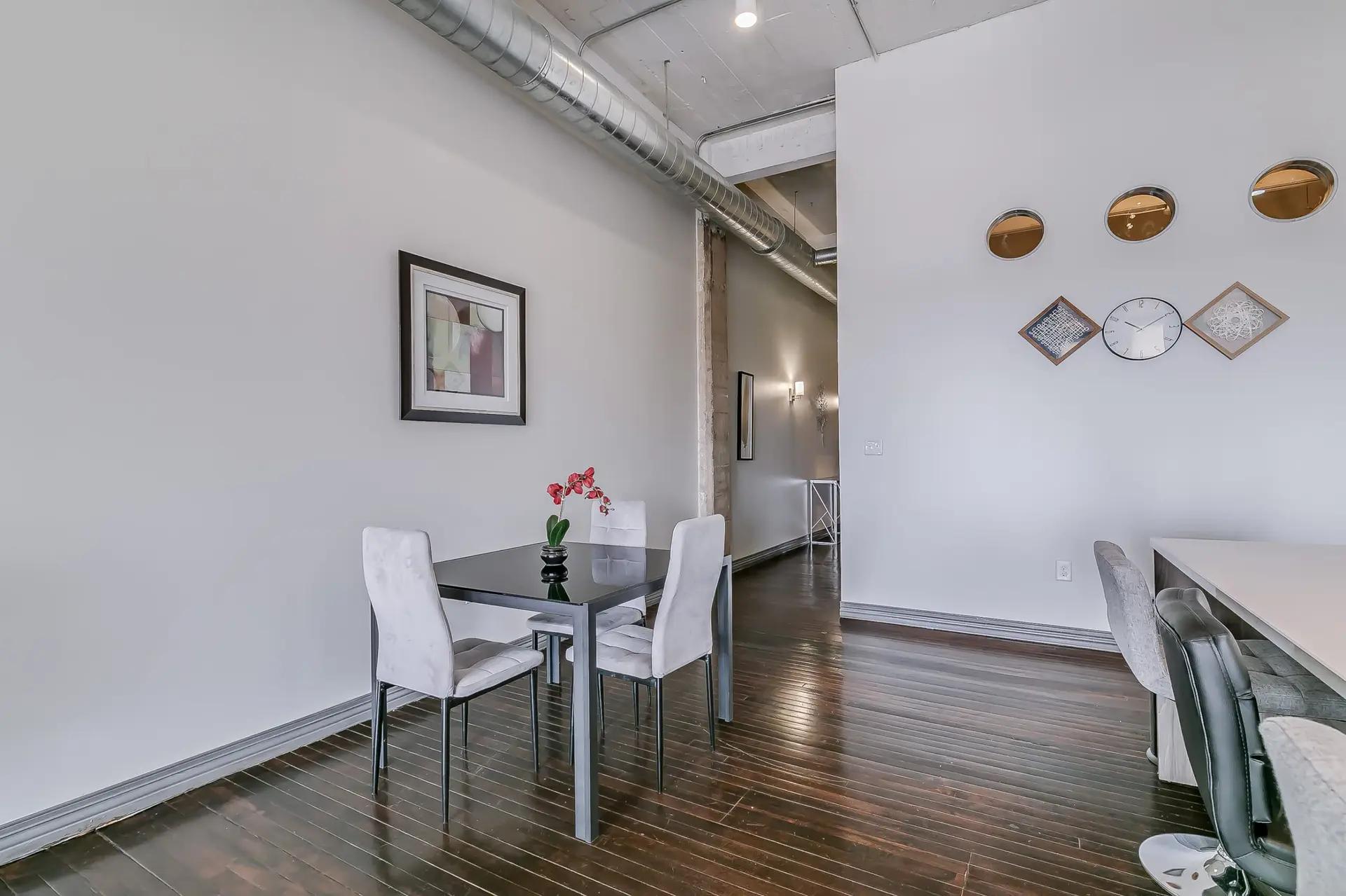 A dining area with a glass-top table and four chairs, near a hallway.
