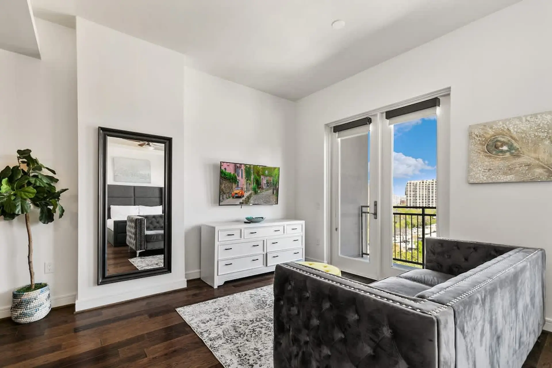 A spacious room with a large mirror, TV, white dresser, and gray couch.