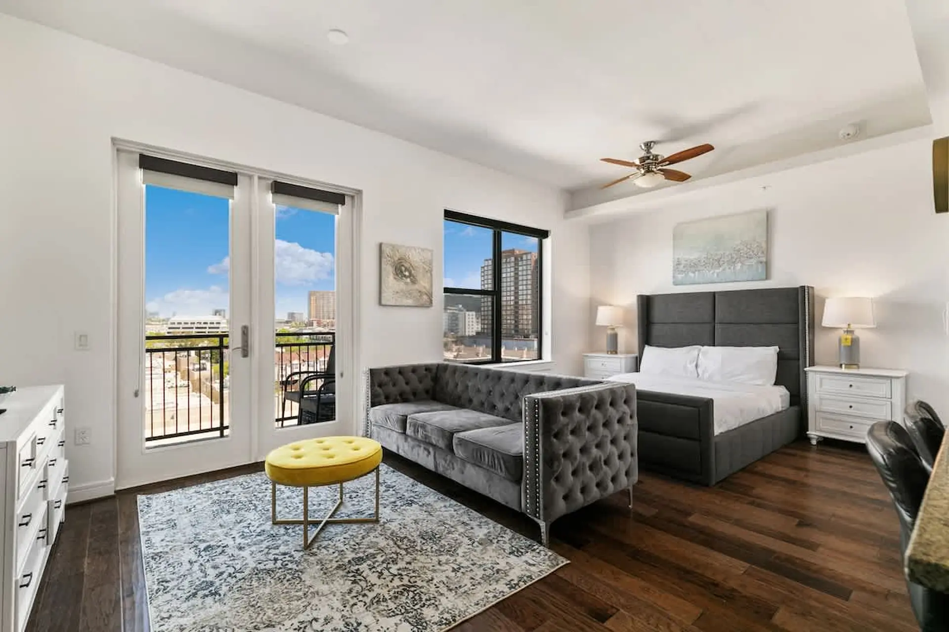 A stylish studio apartment with a bed, sofa, and balcony overlooking a city.