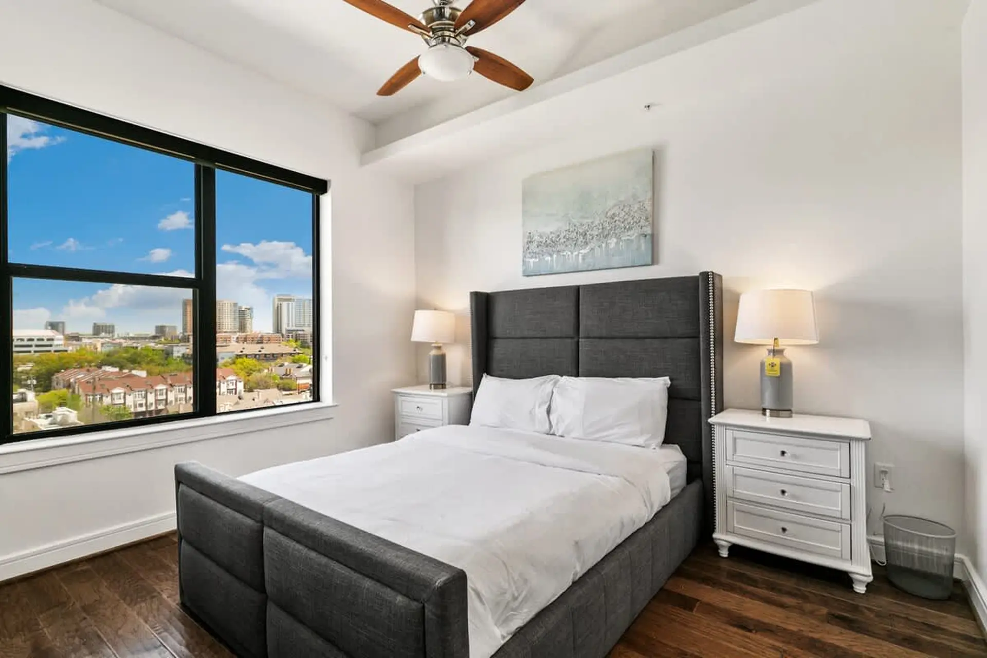 Bedroom with a large window, a bed with a grey headboard, and a ceiling fan.