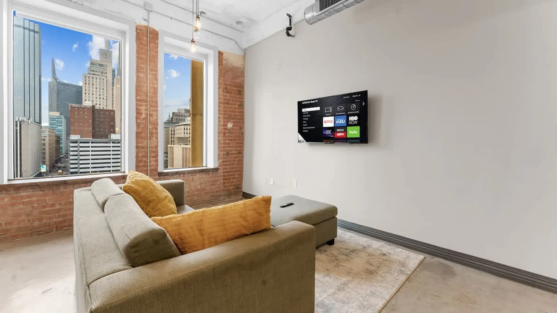 A living room with a couch, ottoman, and TV, overlooking a city skyline.