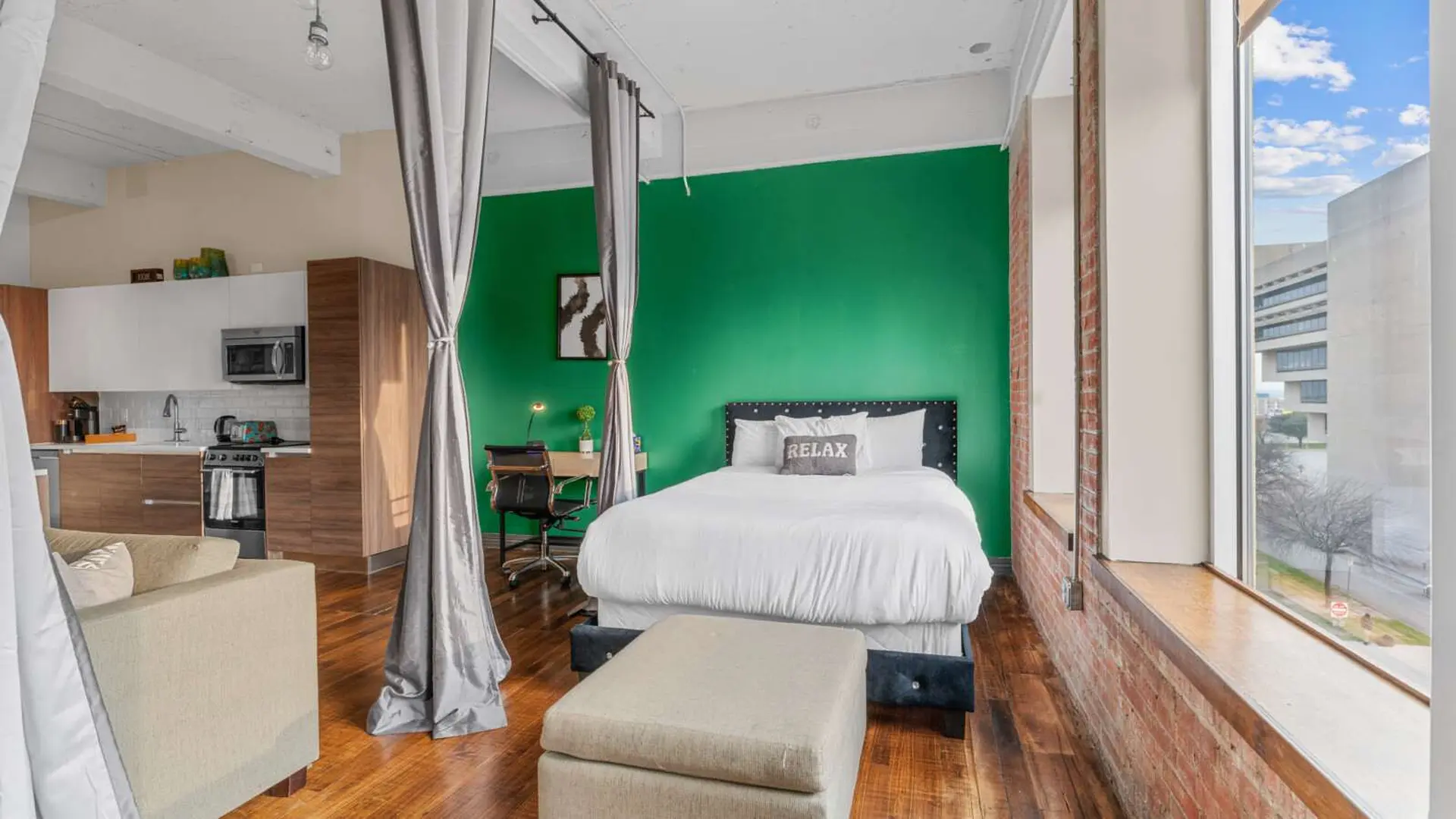 Loft apartment with a kitchen, bed, and desk next to a large window.
