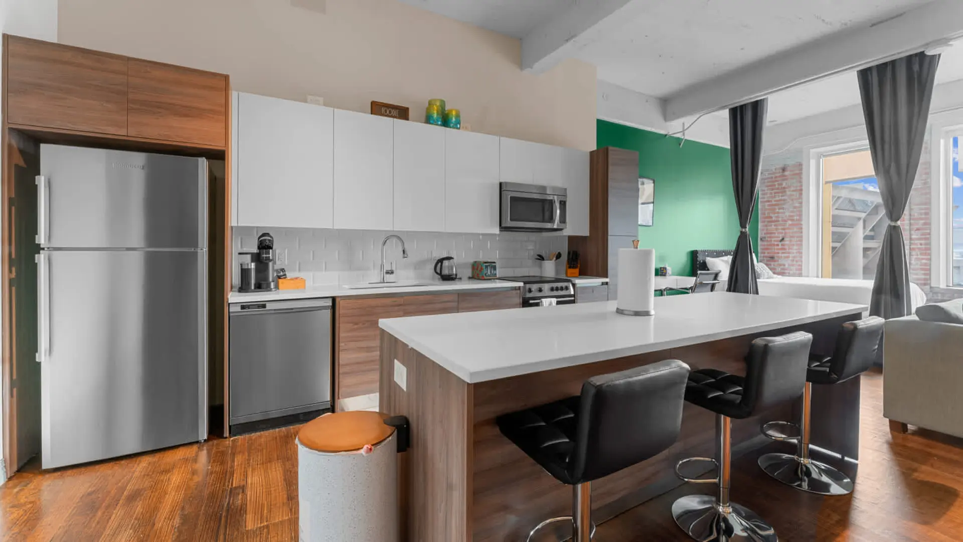 A modern kitchen with stainless steel appliances, white cabinetry, and a breakfast bar with stools.