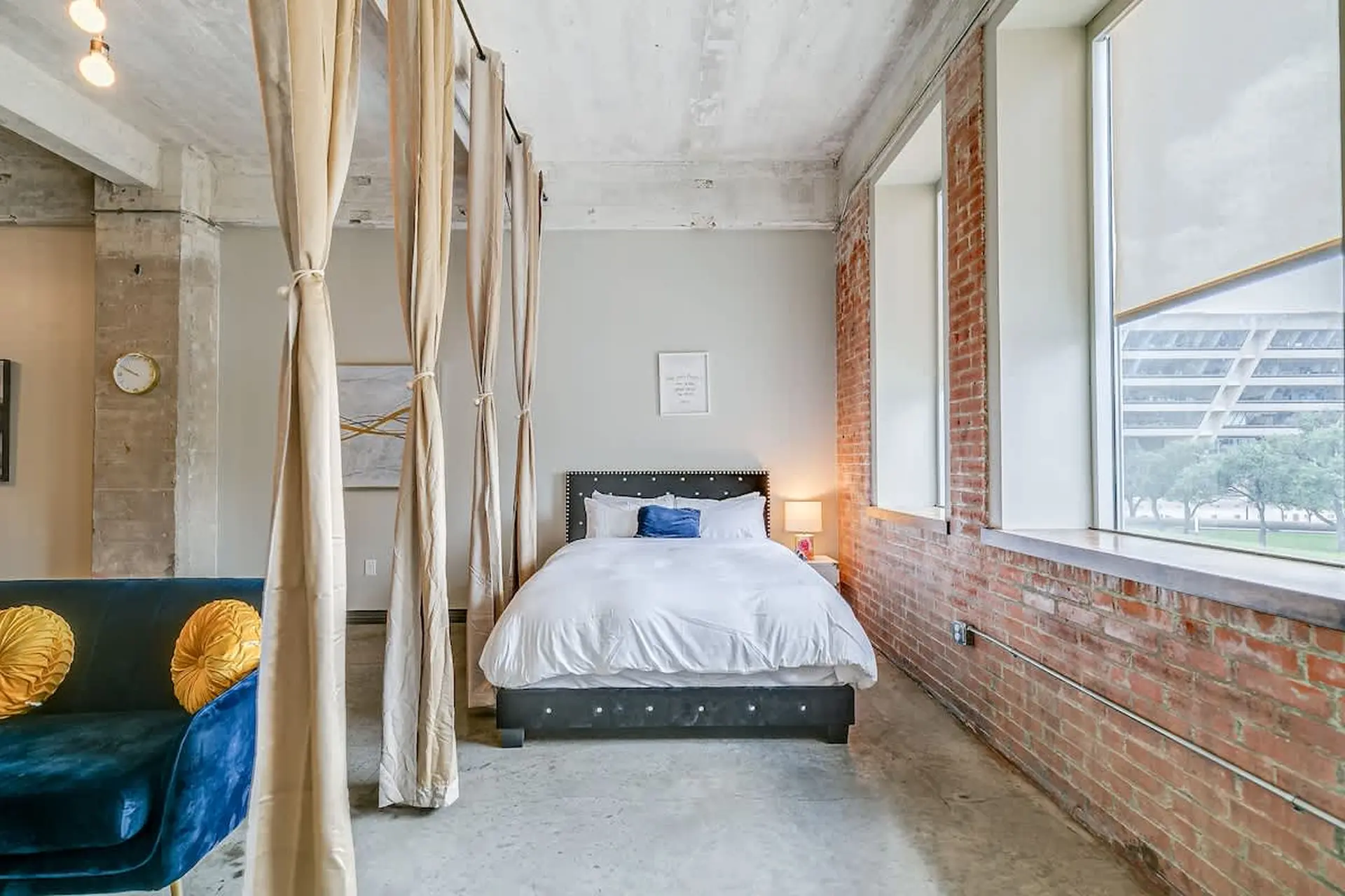 Loft bedroom with bed, couch, curtains, brick wall, and large windows.
