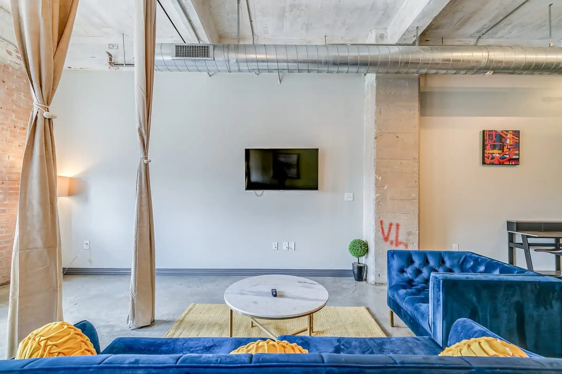 A living room with blue velvet sofas, a marble coffee table, and a TV mounted on the wall.