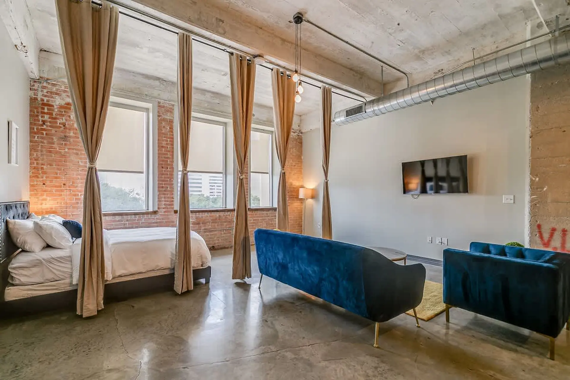 A bedroom and living area with exposed brick walls, concrete floors, and industrial-style decor.