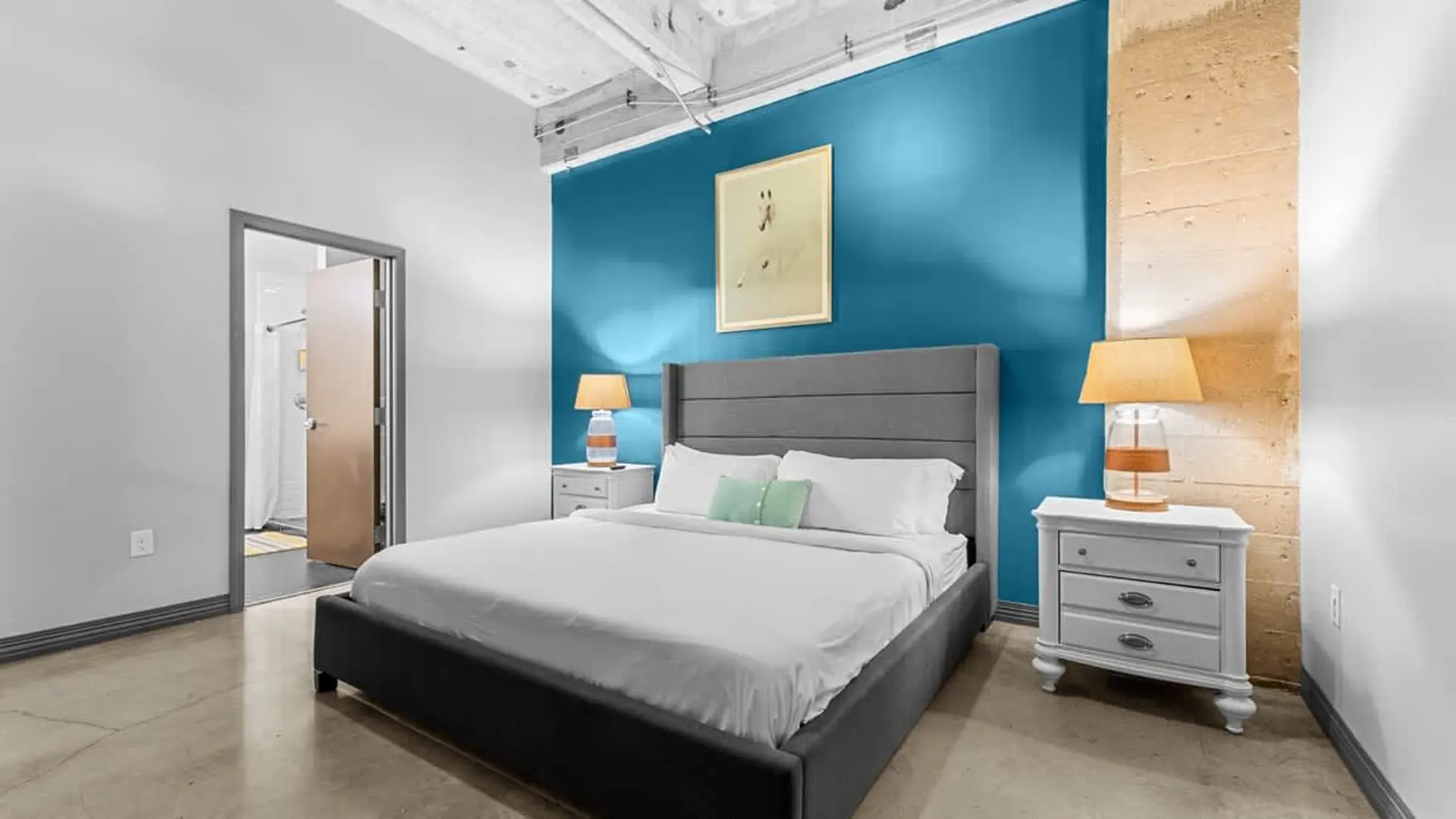 A bedroom with a king-size bed, teal accent wall, and industrial-style ceiling.