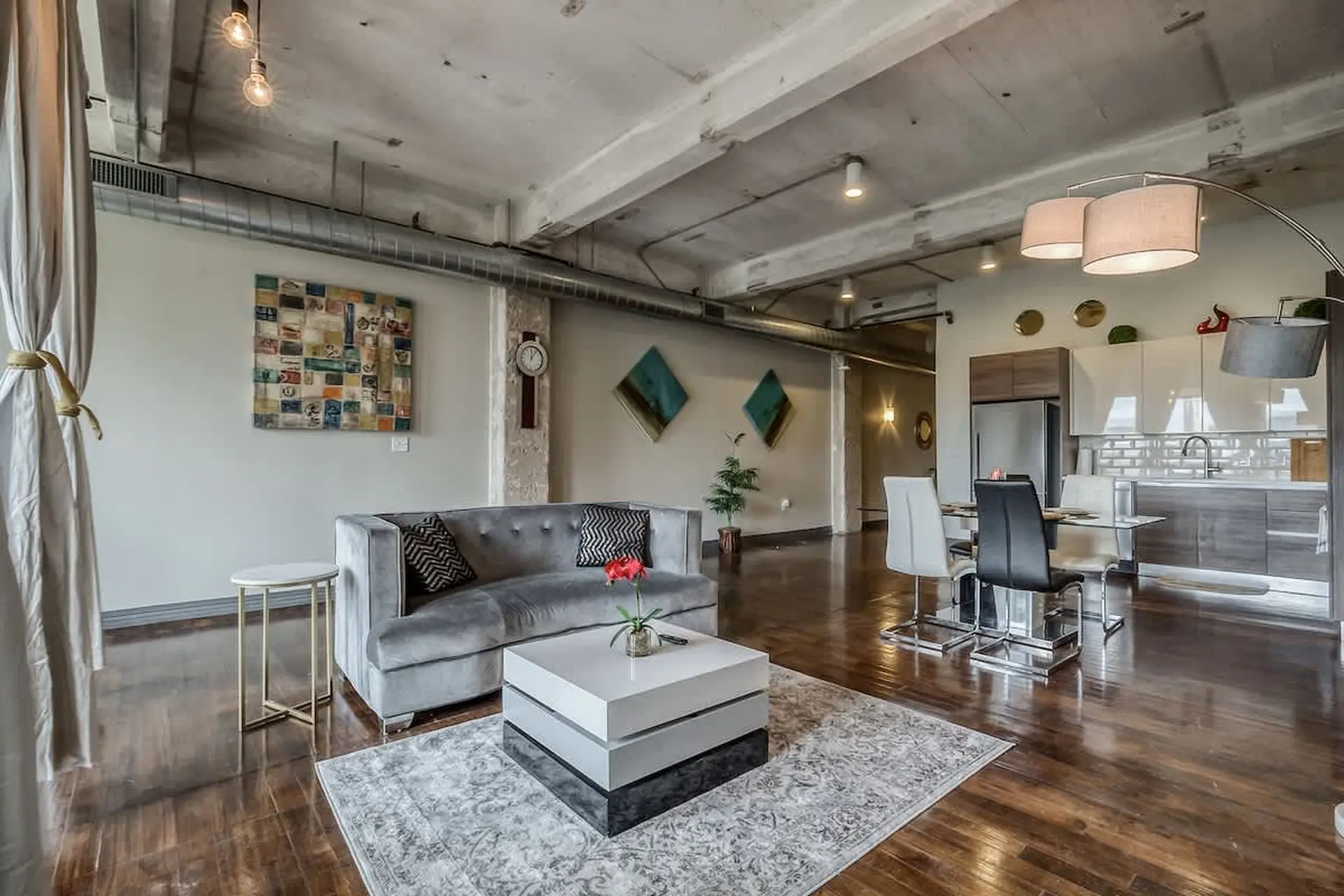 Loft living room and kitchen with grey velvet sofa, modern coffee table, and dining area.
