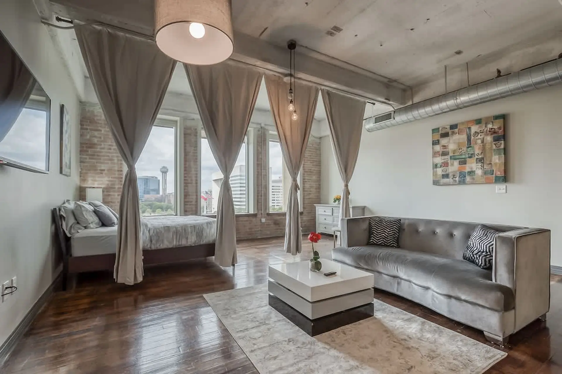 Loft apartment bedroom with bed, sofa, coffee table, and city view.