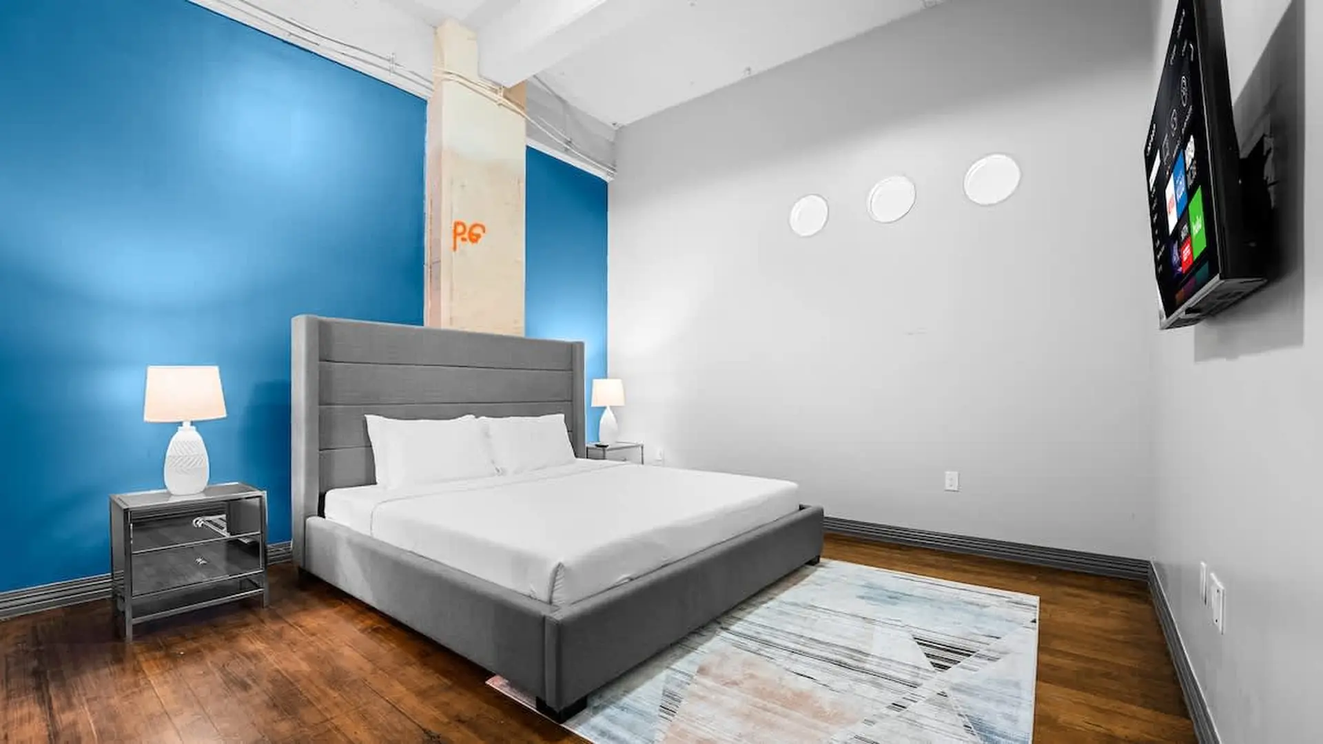 A modern bedroom with a gray bed, blue wall, and a tv.