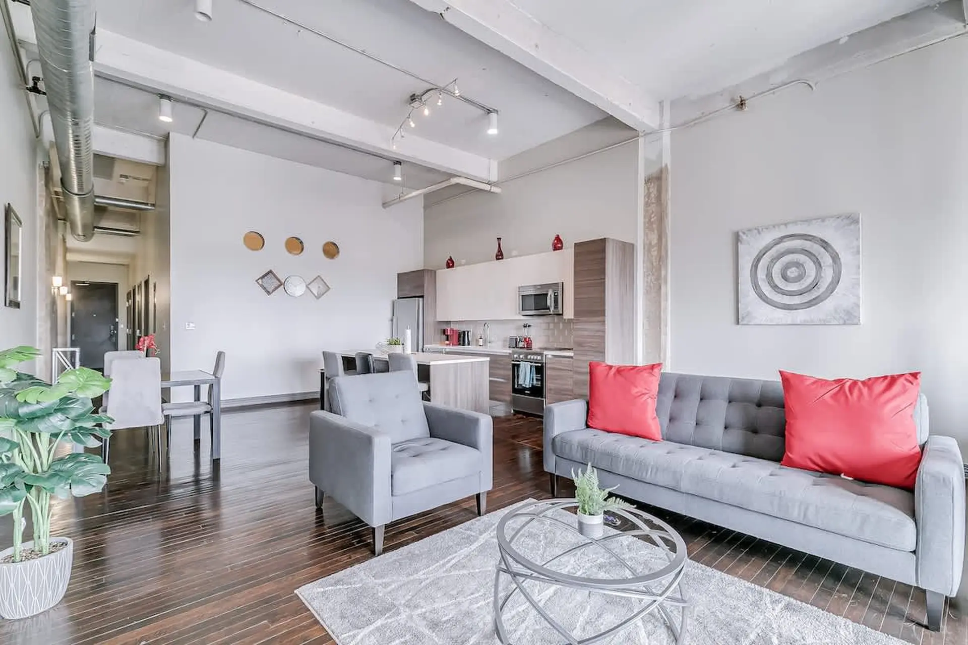 A modern living room with a gray sofa and armchair, accented by red pillows.