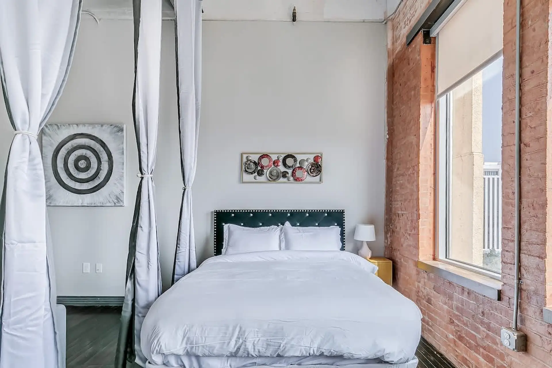 A bed with white linens is in front of a teal tufted headboard.