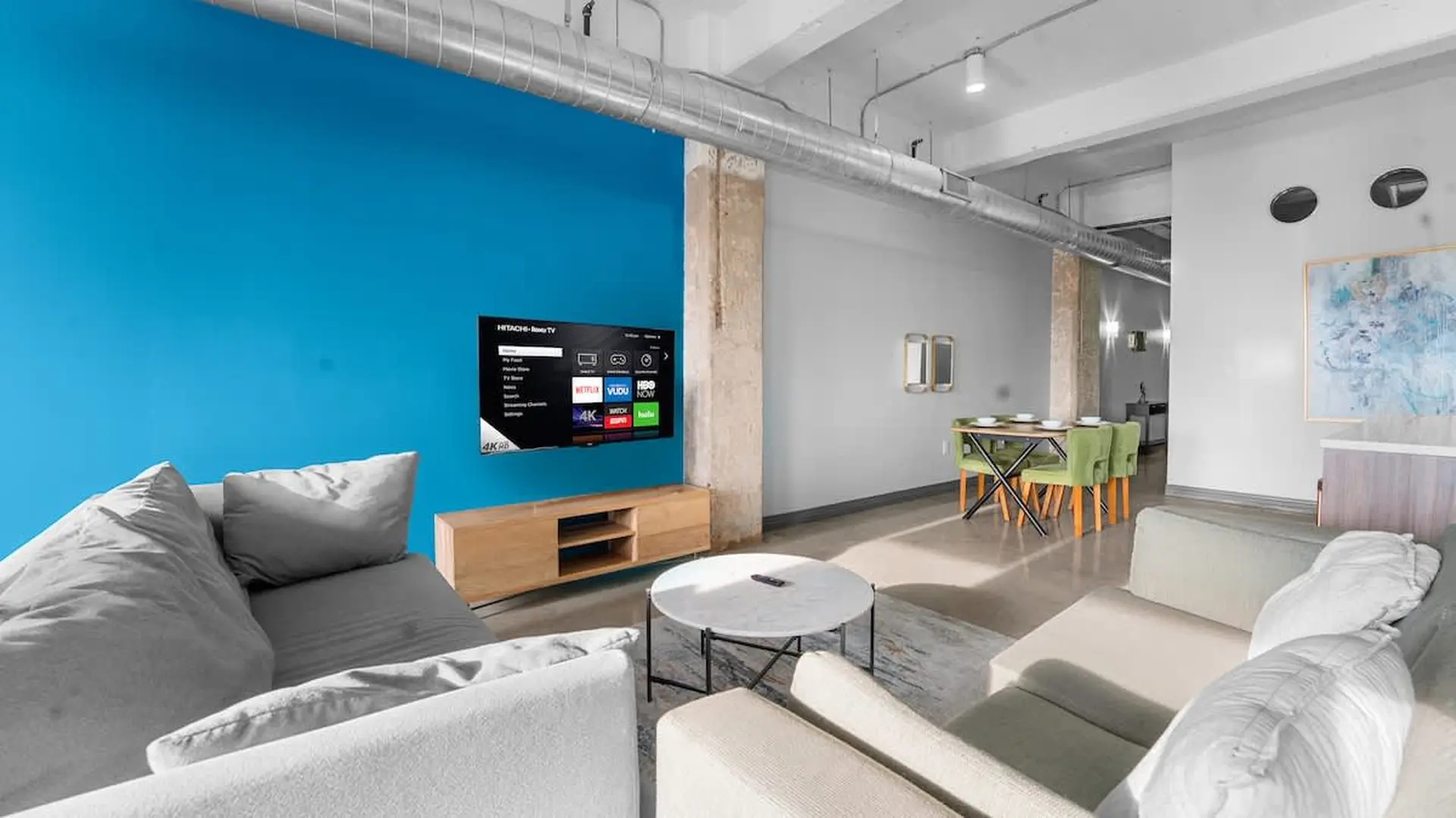 Modern living room with blue accent wall, television, couch, coffee table, and dining area.