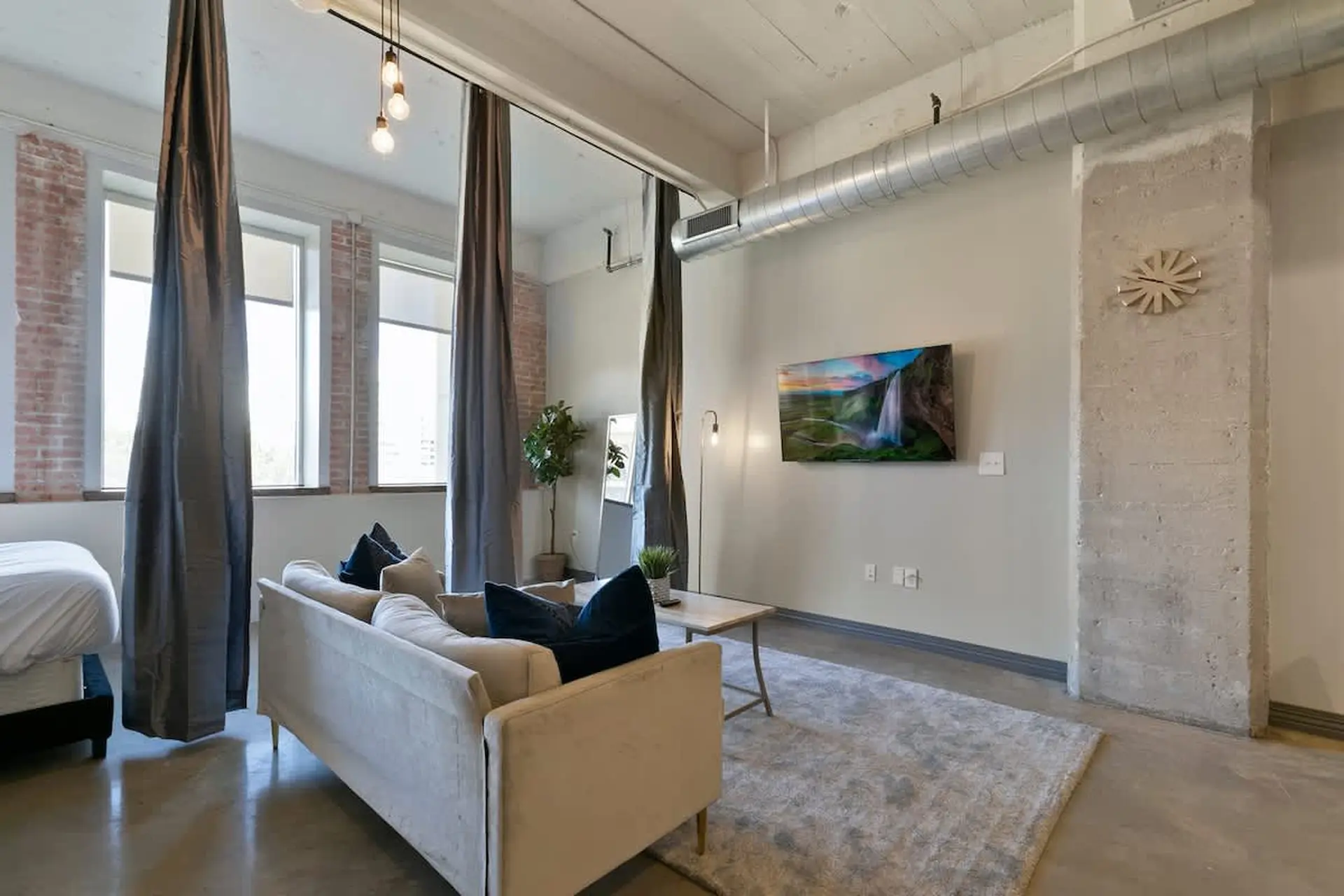 A modern loft living area with a sofa, coffee table, and a TV displaying a waterfall.