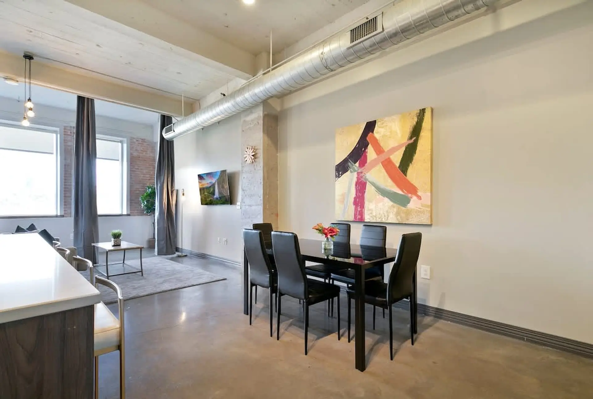 A dining table with chairs and a painting hang on the wall.