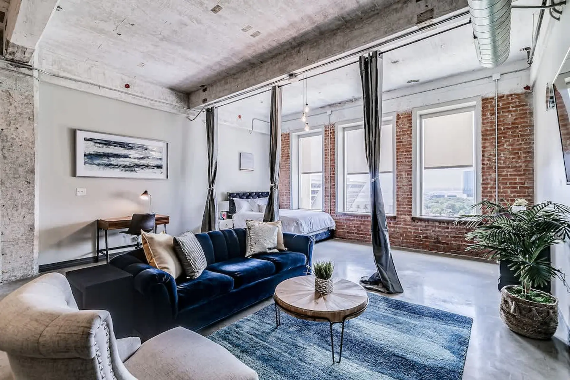 Loft bedroom with blue couch, brick walls, and large windows.