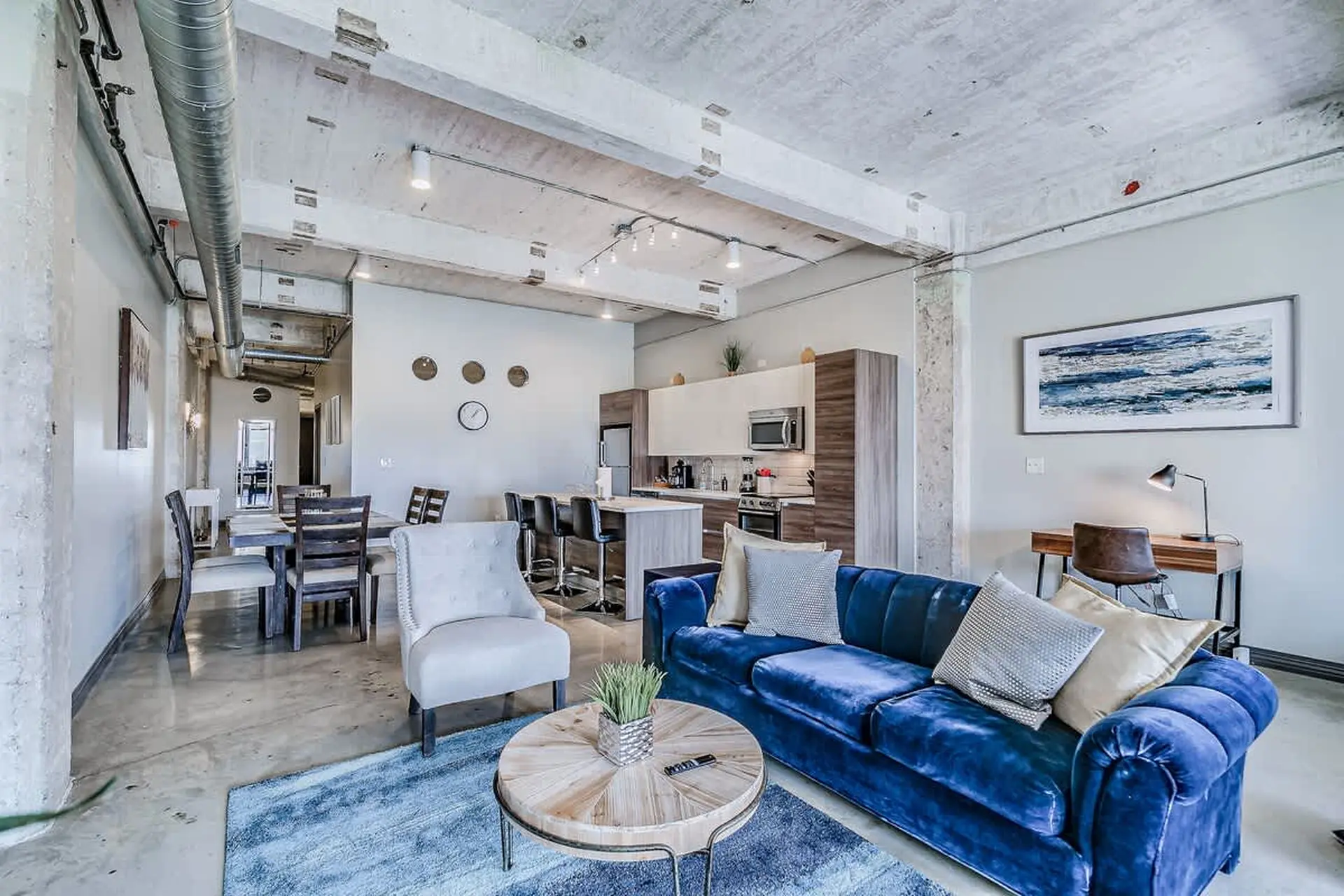 A modern living room with blue couch, dining table, and kitchen island.