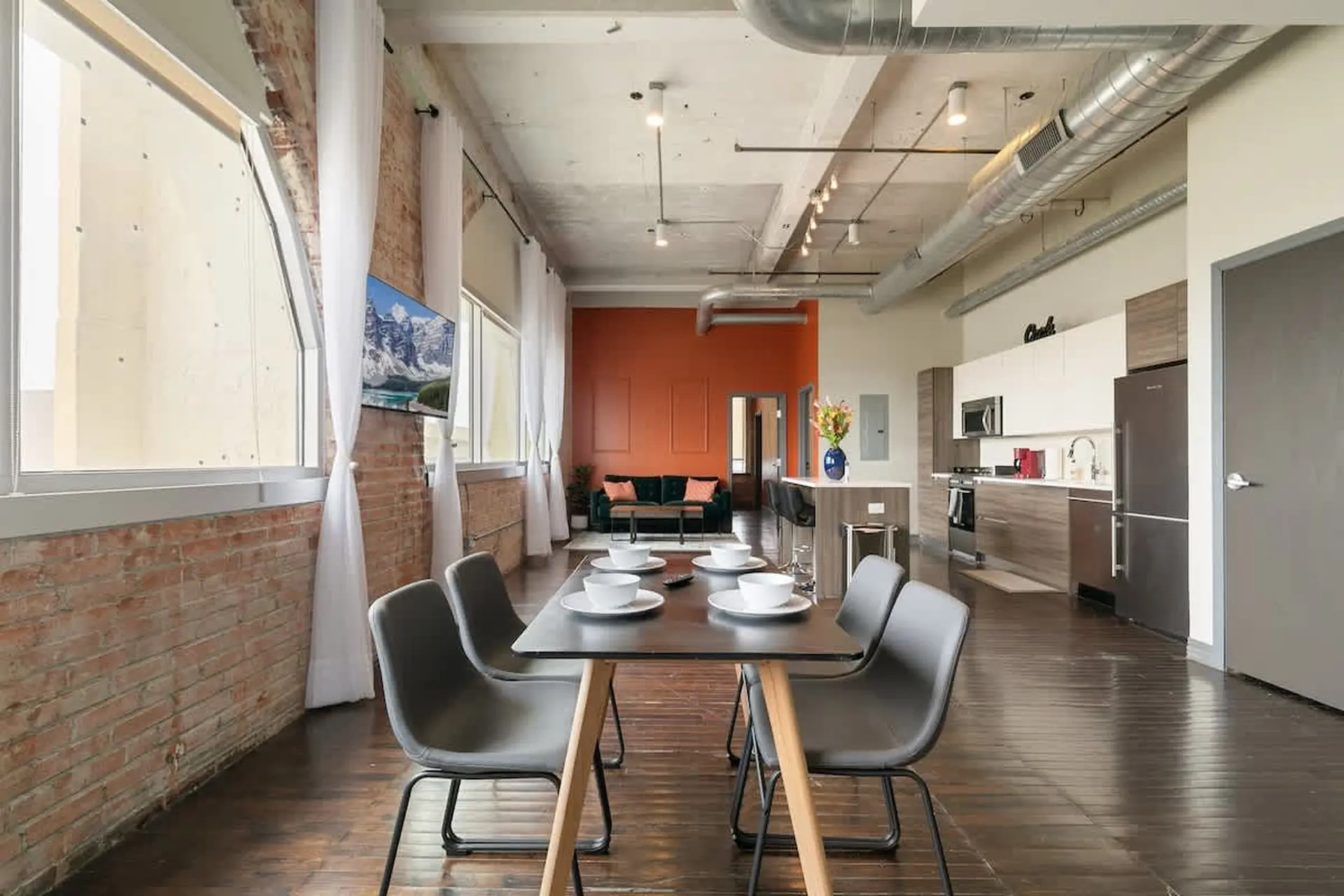 Loft living room with brick walls, large windows, and open-concept kitchen and dining area.