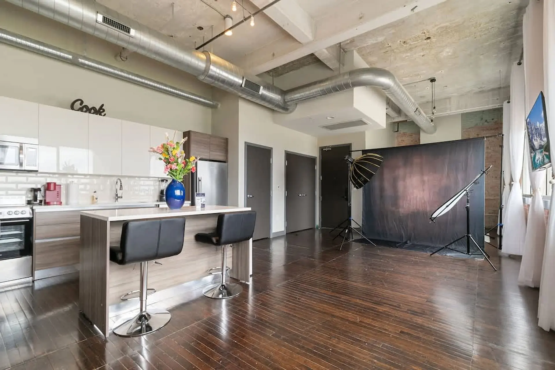 Modern kitchen with island, stools, and photography studio backdrop.