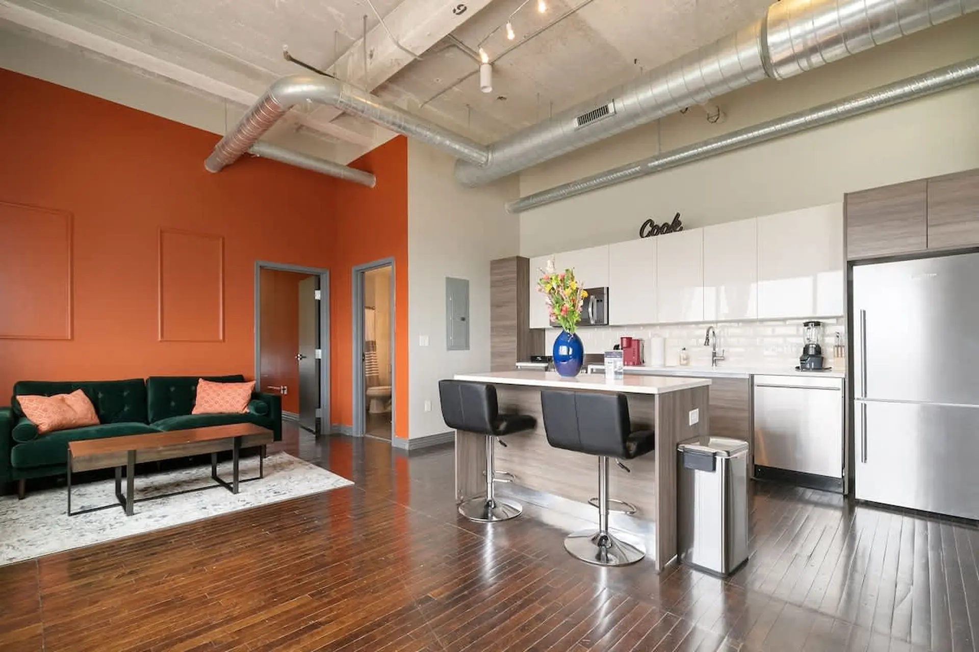 Loft living room and kitchen with an orange wall, green sofa, and stainless steel appliances.