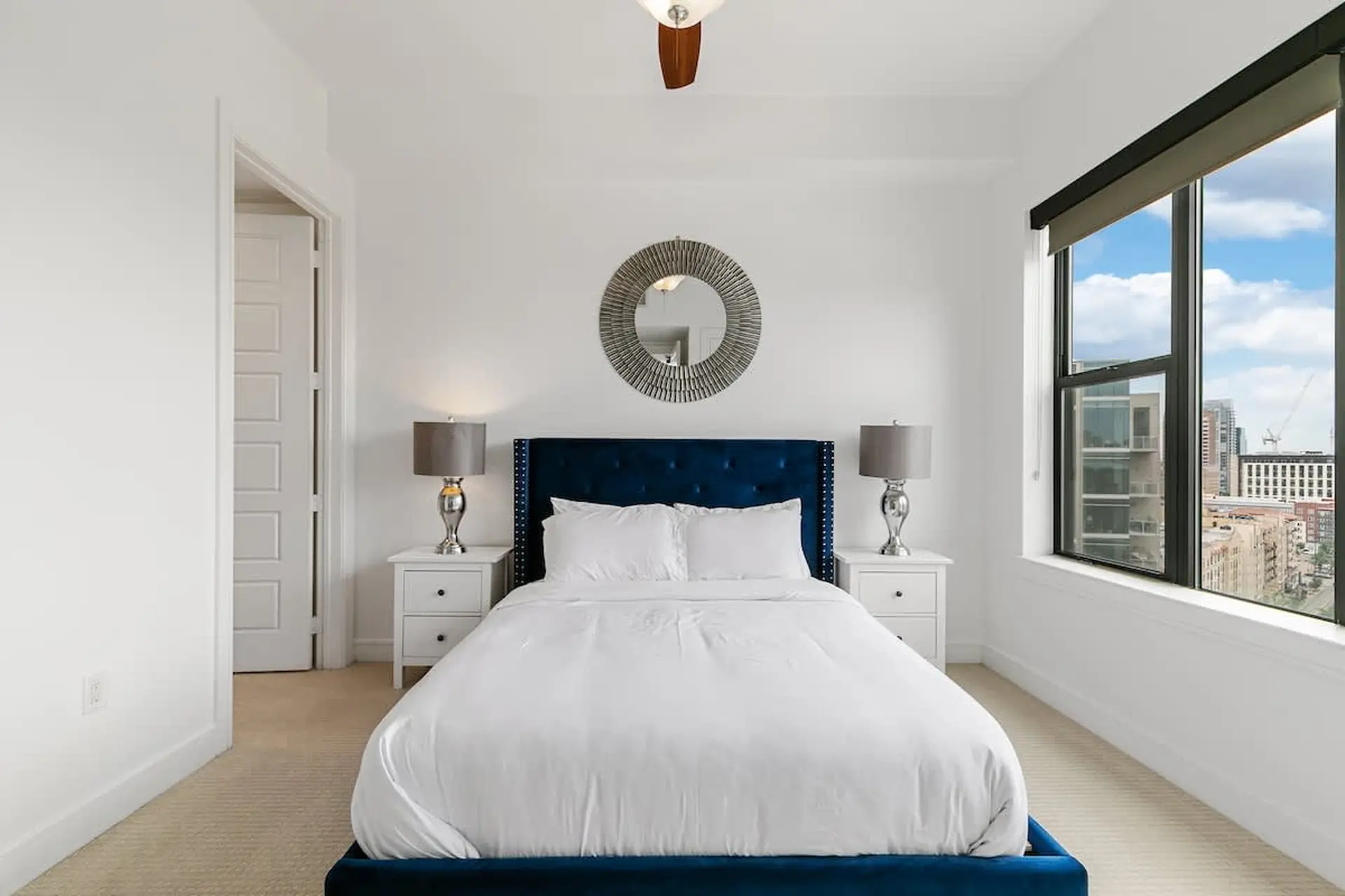 A bedroom with a blue tufted headboard, white bedding, and bedside tables.