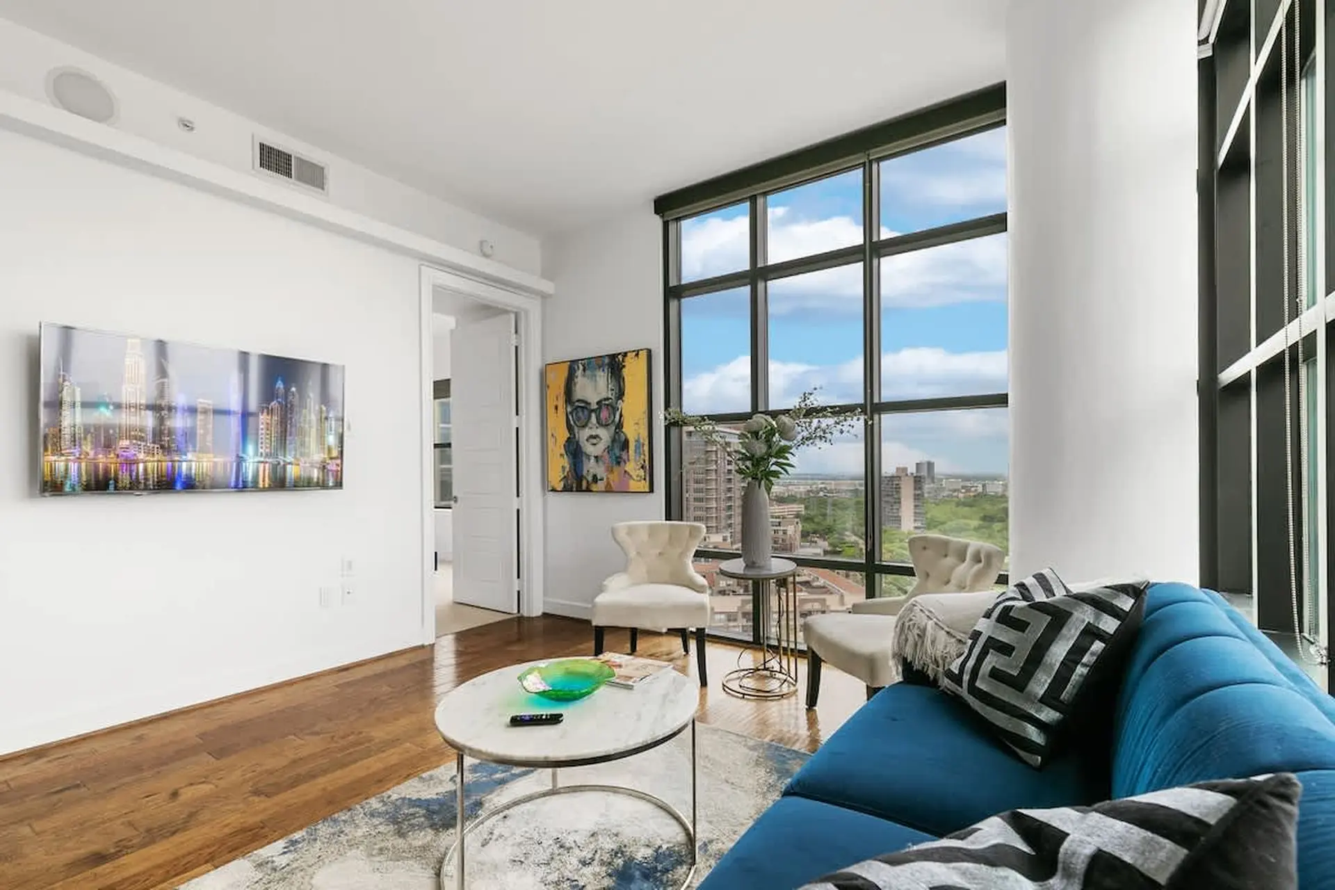 A modern living room with a blue sofa, marble coffee table, and cityscape view.