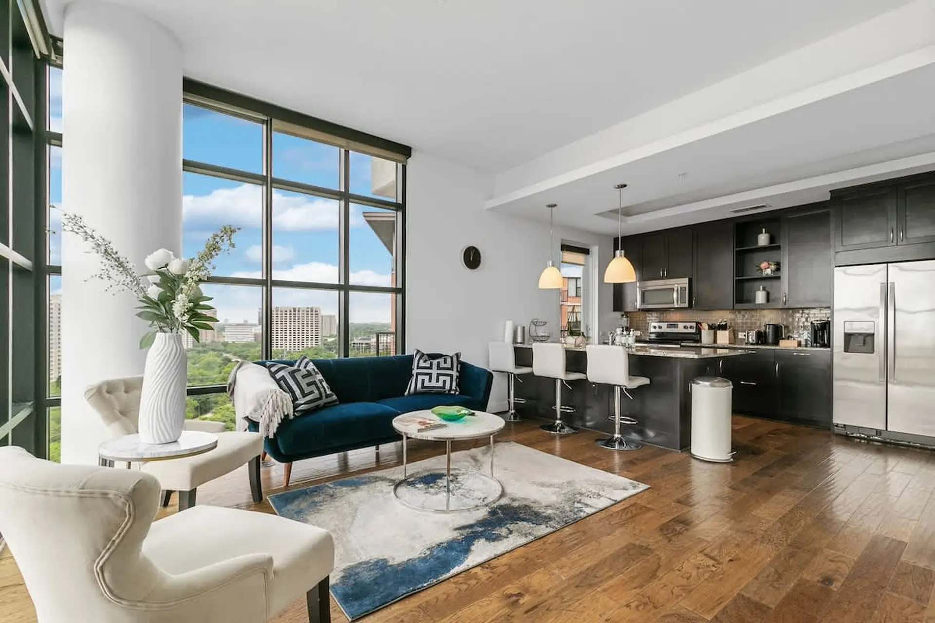 A modern living room and kitchen with large windows offering a city view.