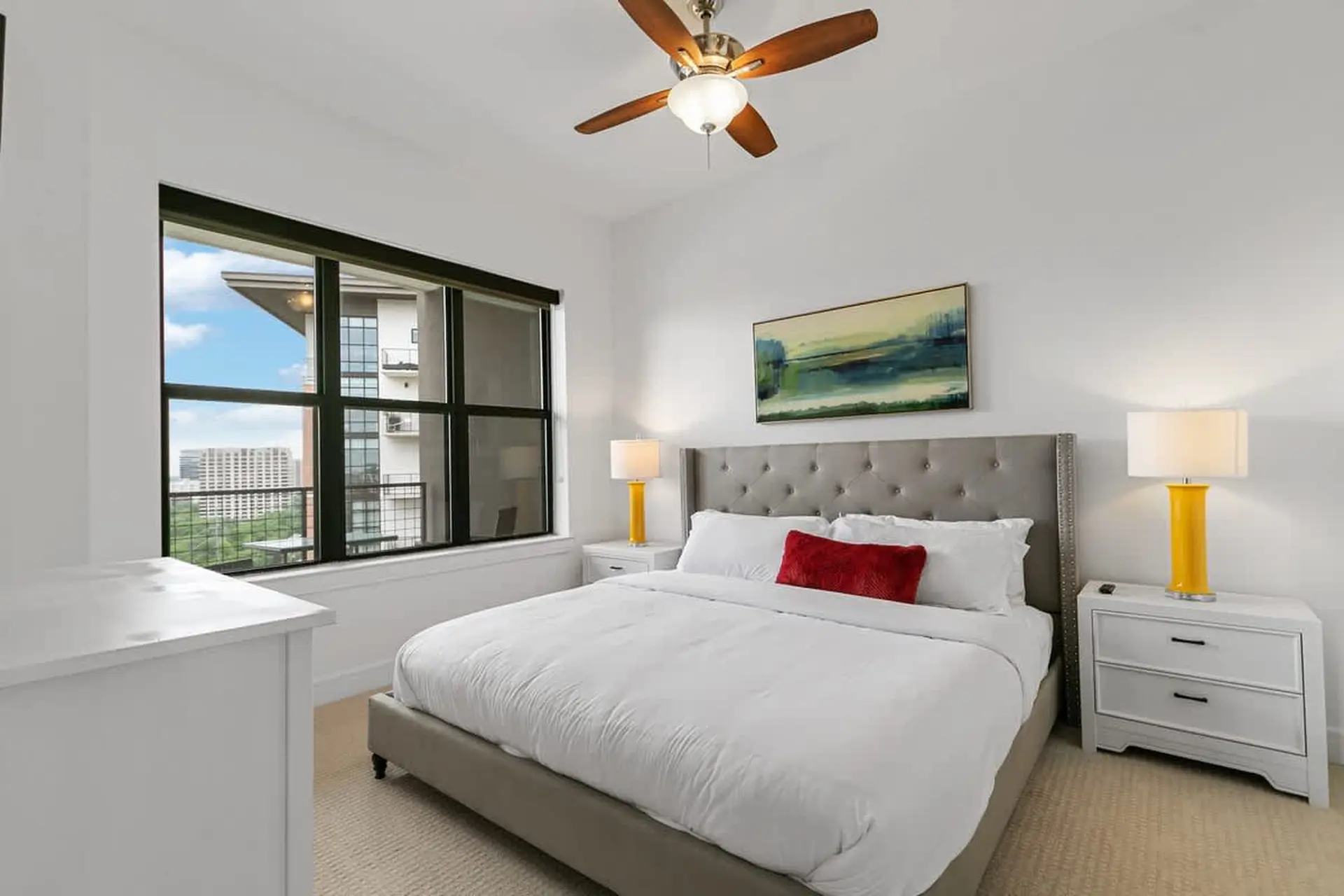 A bedroom with a bed, nightstands, a painting, and a ceiling fan.