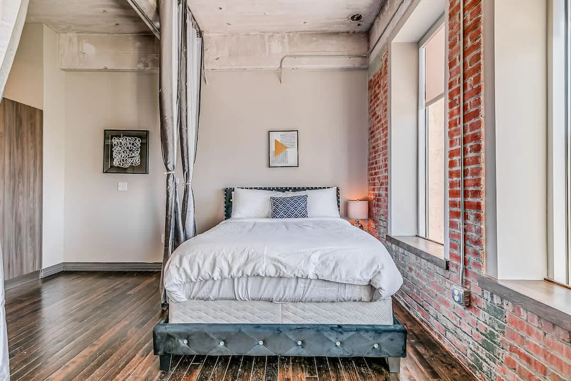 Bedroom with exposed brick, large windows, and a plush bed.