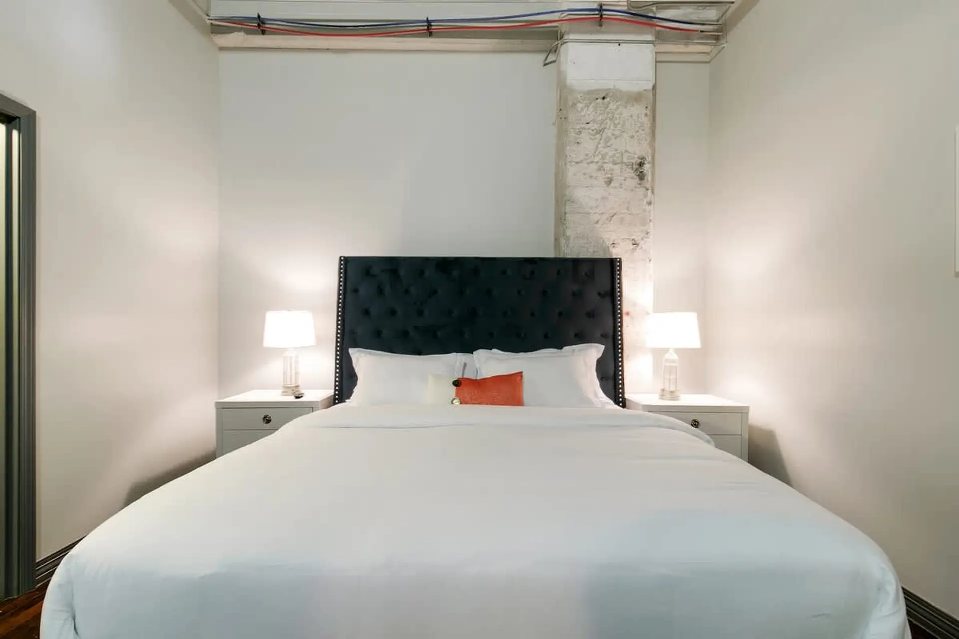 A minimalist bedroom with a white bed and a dark tufted headboard.