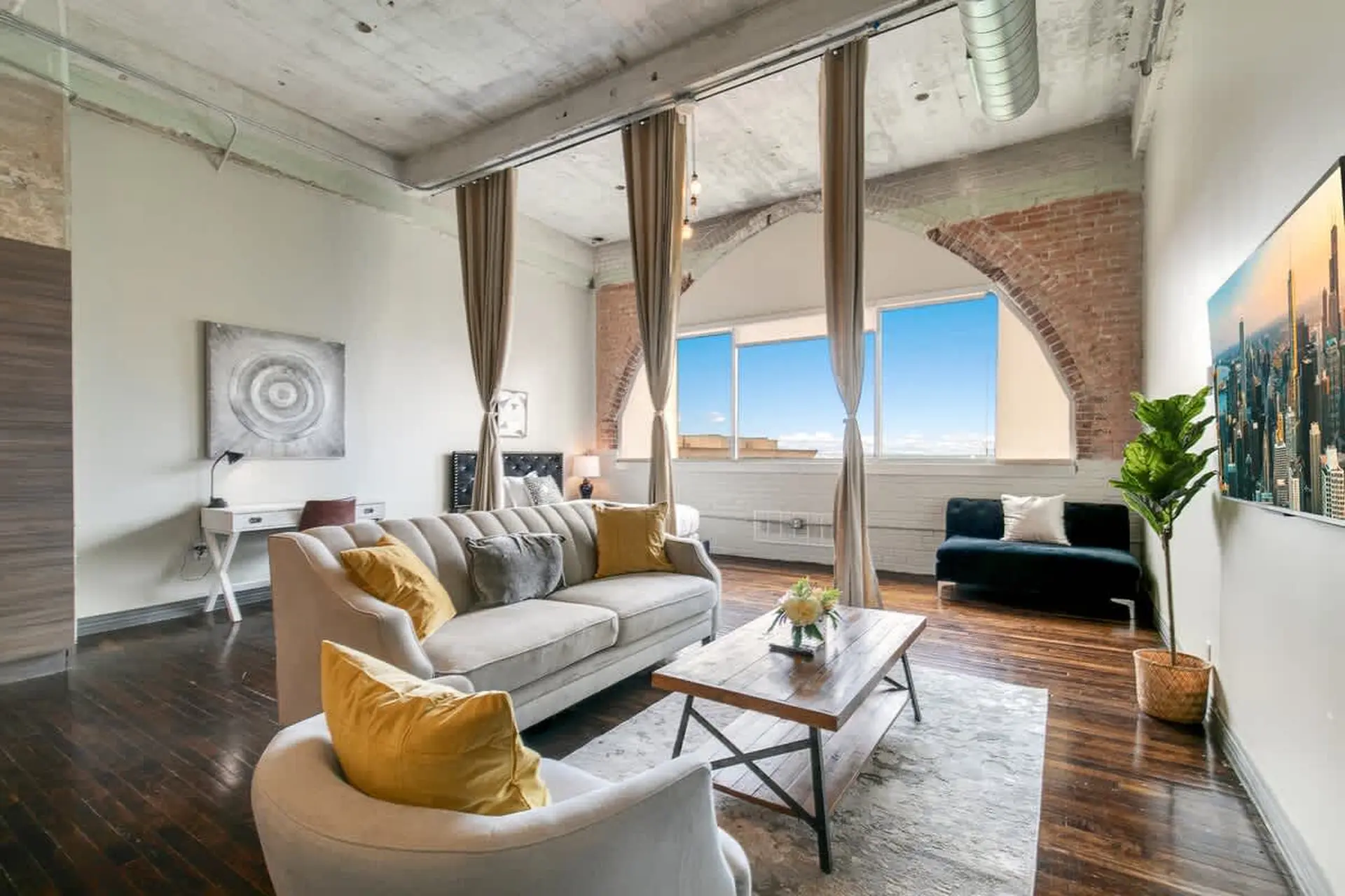 Living room with couch, coffee table, desk, and large windows.