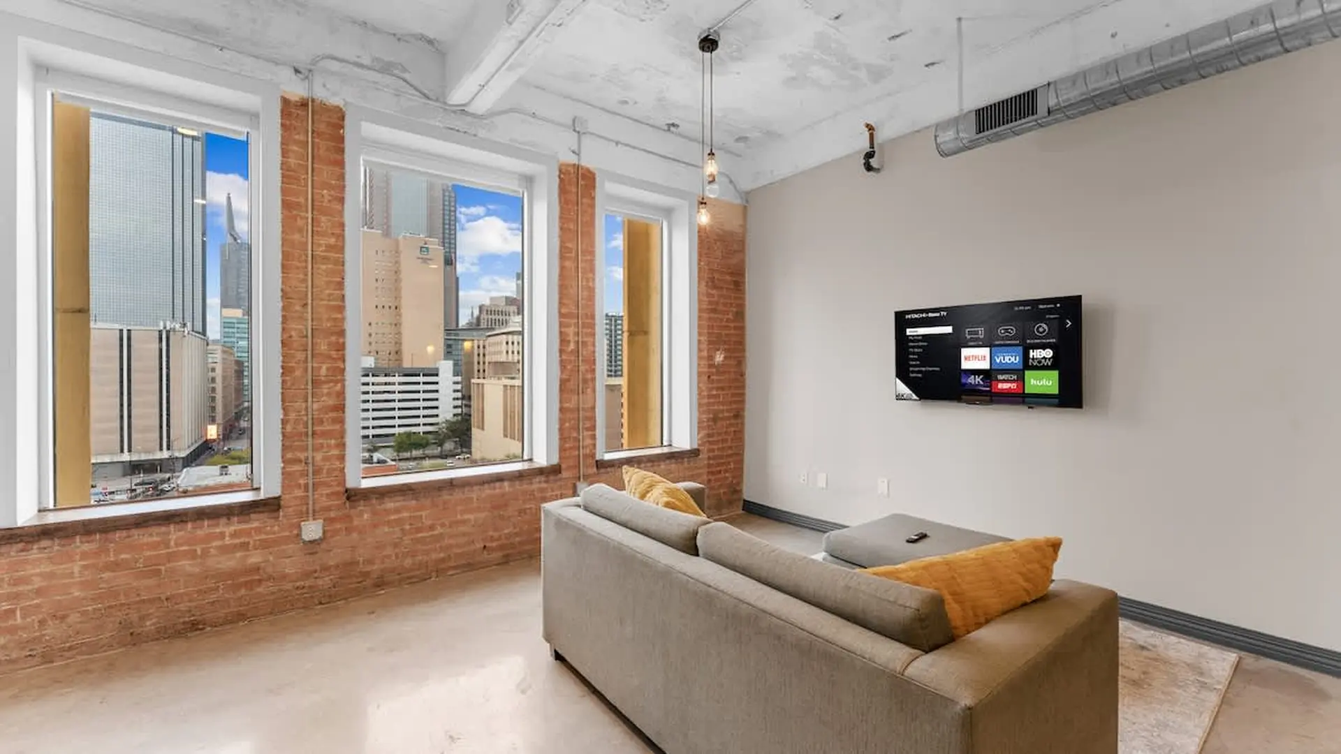 Living room with a brick wall, large windows, and a TV mounted on the wall.