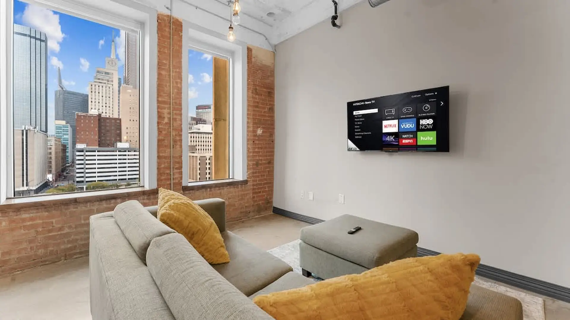 A modern living room with a sectional sofa, ottoman, and a TV mounted on the wall.