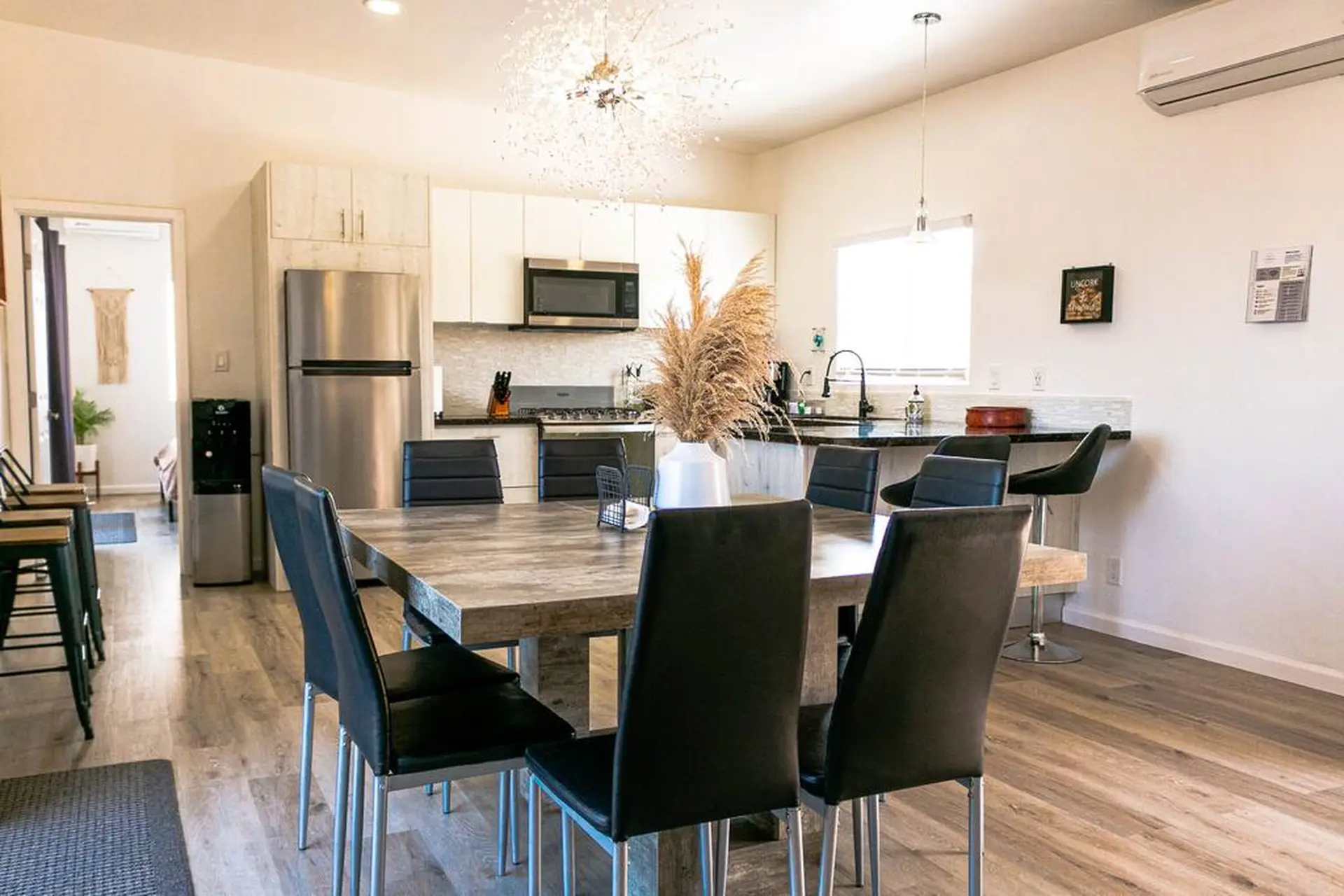 A dining room and kitchen with a chandelier, refrigerator, and microwave.
