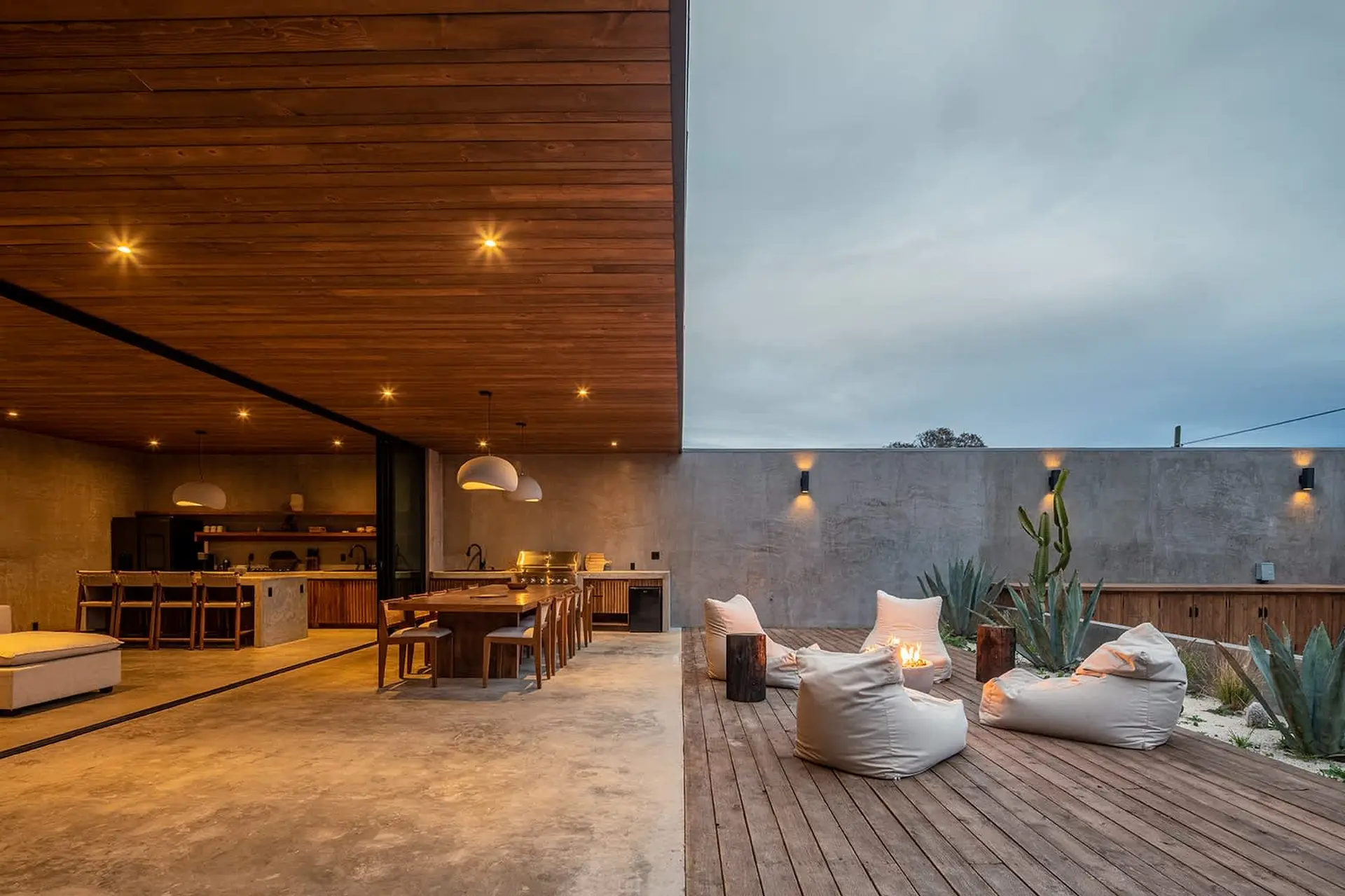 A modern outdoor dining and lounge area with a fire pit and beanbag chairs.
