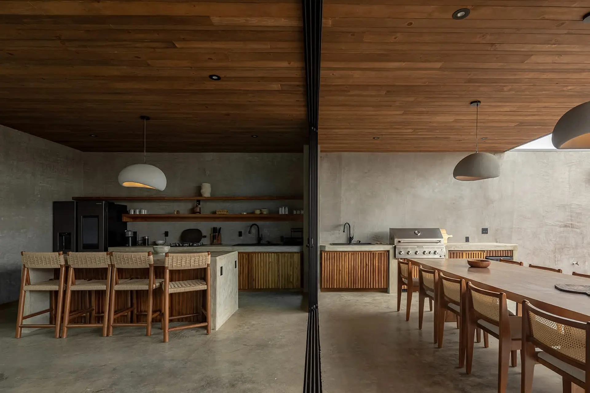 A modern open-plan kitchen and dining area with concrete floors and wooden accents.