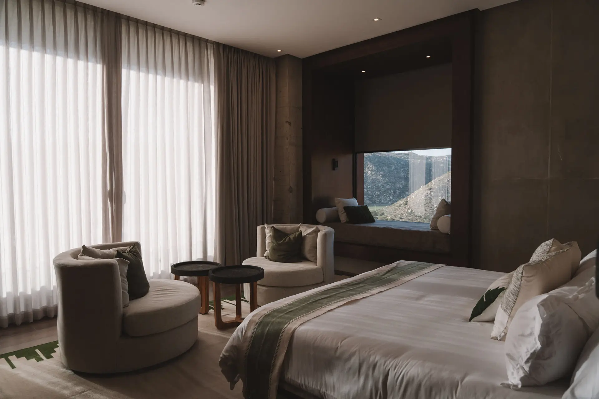 A modern bedroom with curved chairs, side tables, and a bed with a view.