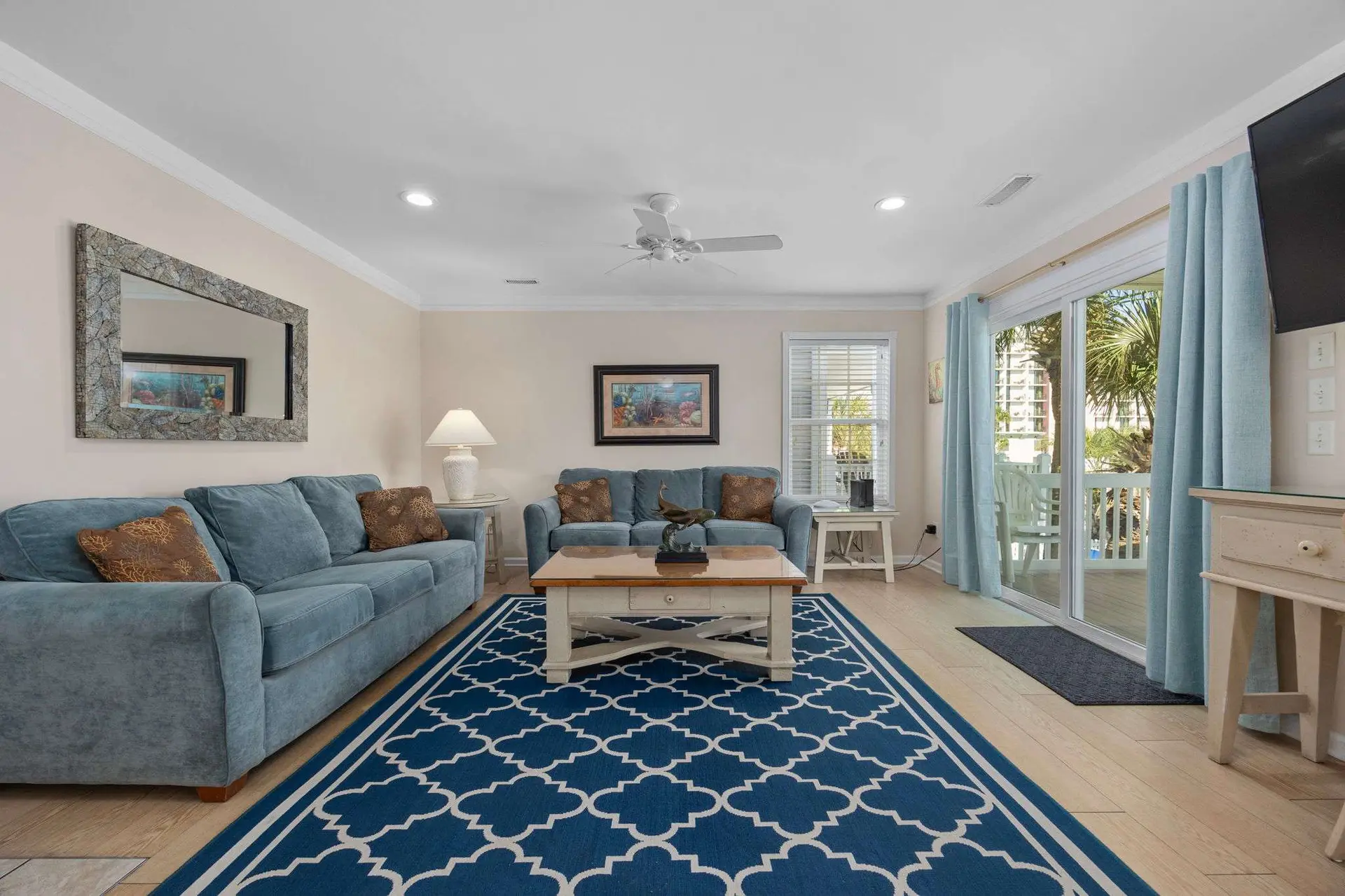 Living room with blue sofas, coffee table, rug, and a sliding glass door to an outdoor patio.