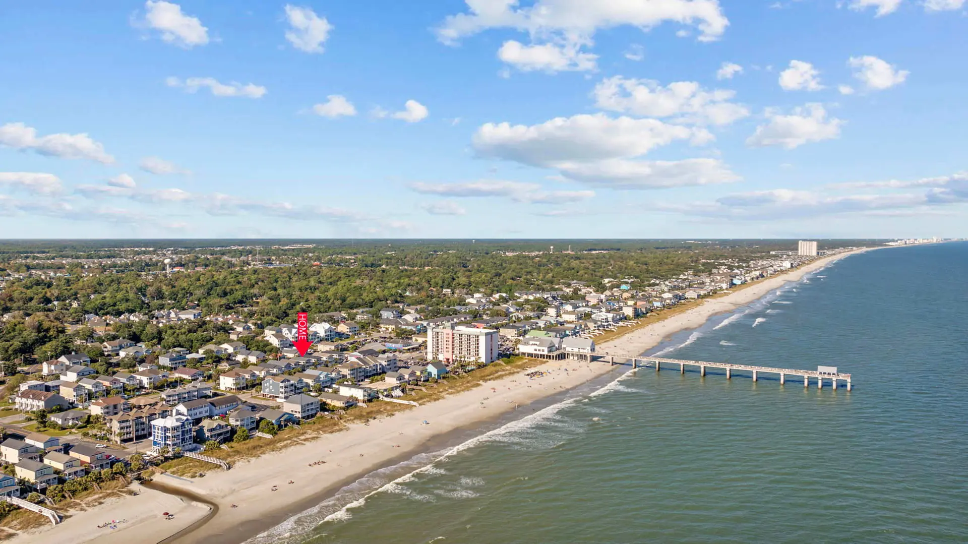 Aerial view of a beach town with homes, a pier, and the ocean.